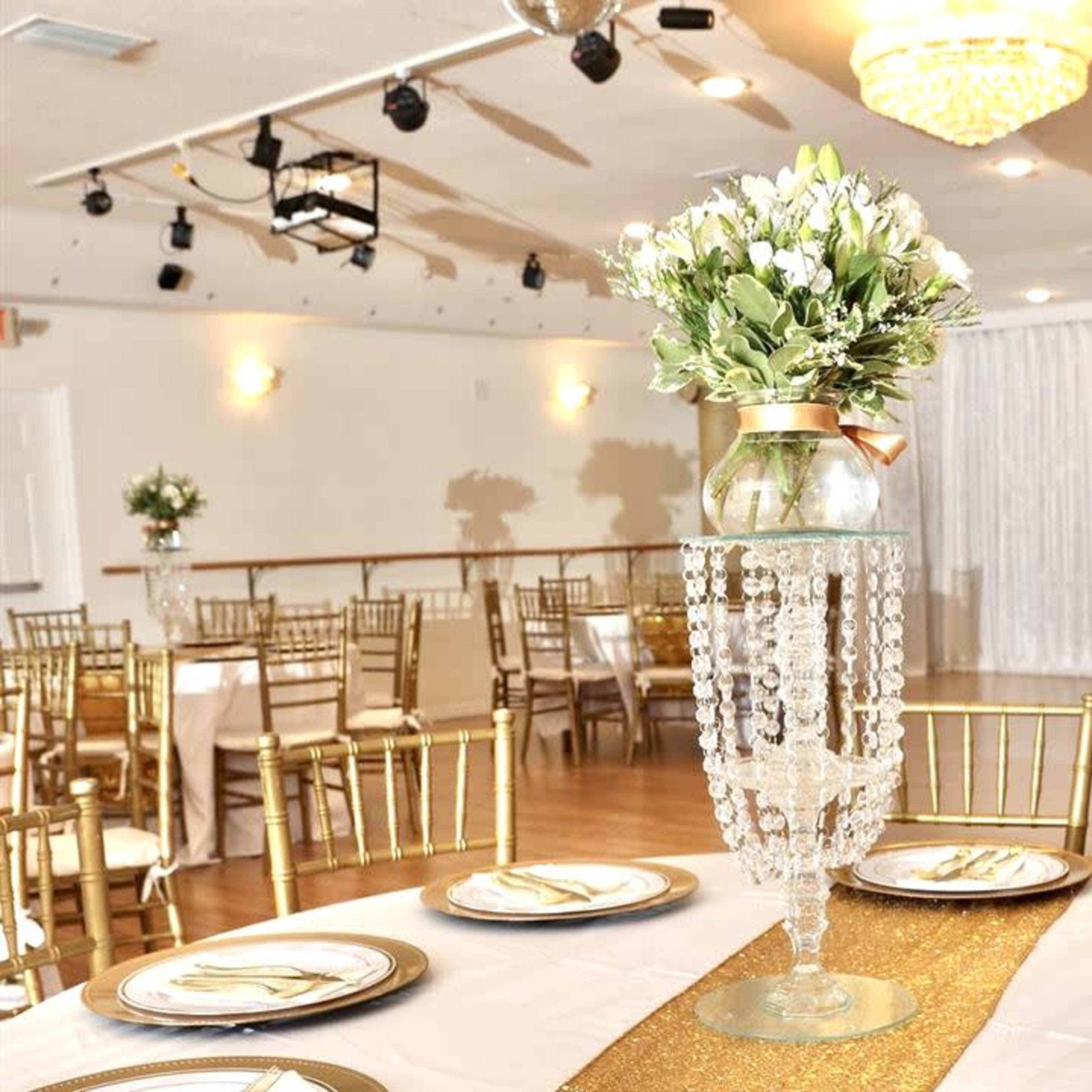 A banquet hall is set up for an event with round tables adorned with elegant centerpieces and golden chairs.