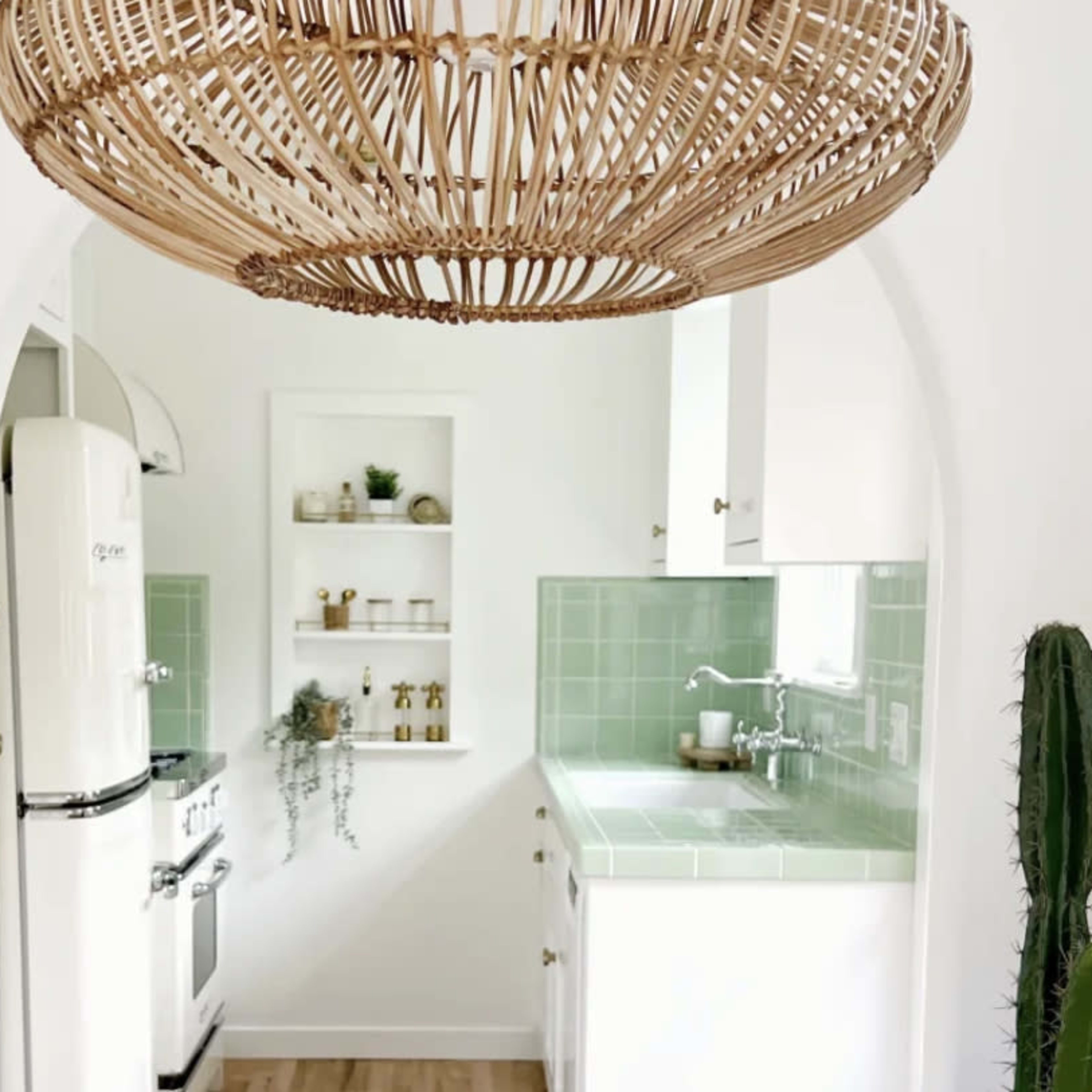 A kitchen is visible through an archway, featuring a retro fridge, green tiled backsplash, and a large woven light fixture overhead.