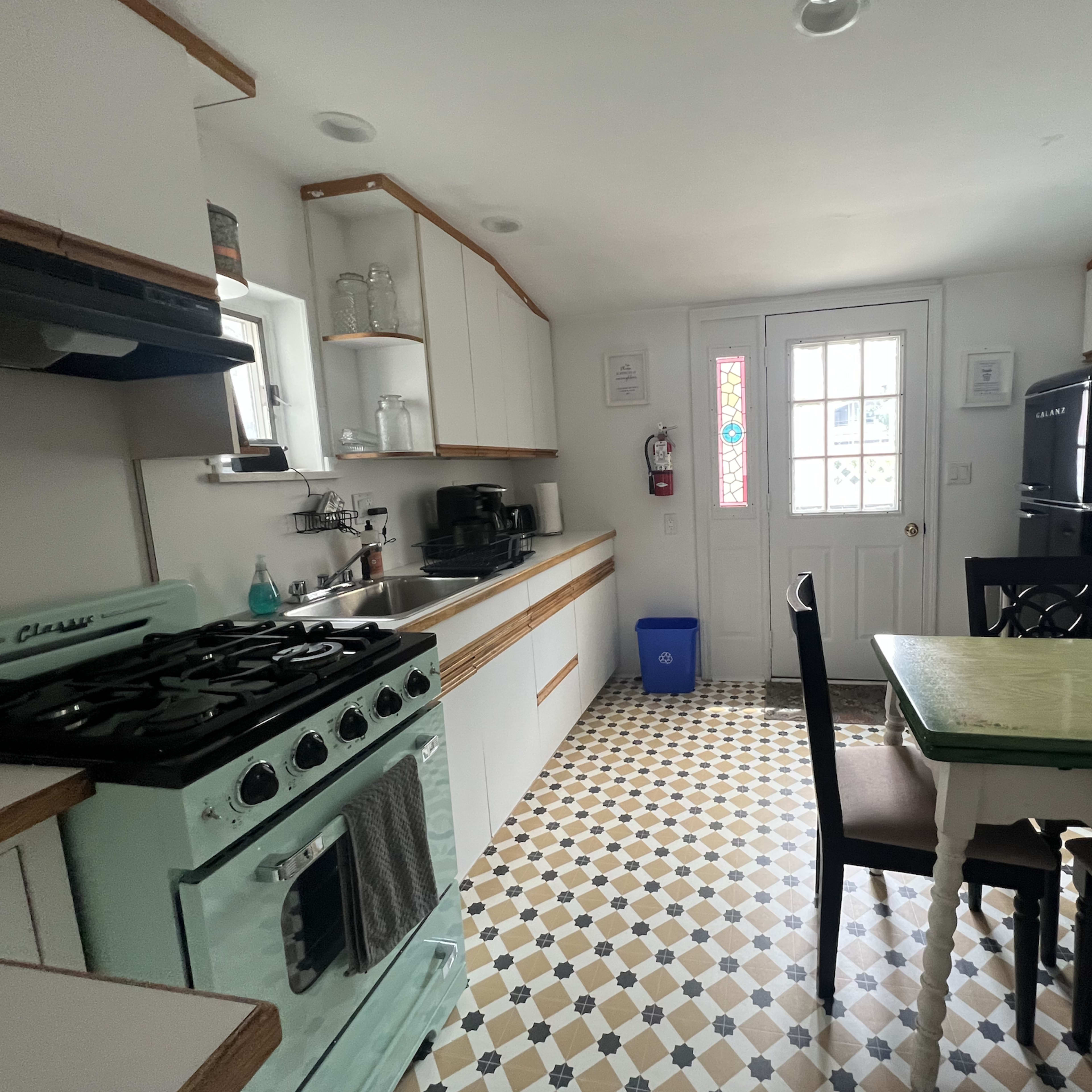 A compact kitchen featuring a vintage-style aqua stove, a black refrigerator, a dining table with chairs, and a door with a glass panel.