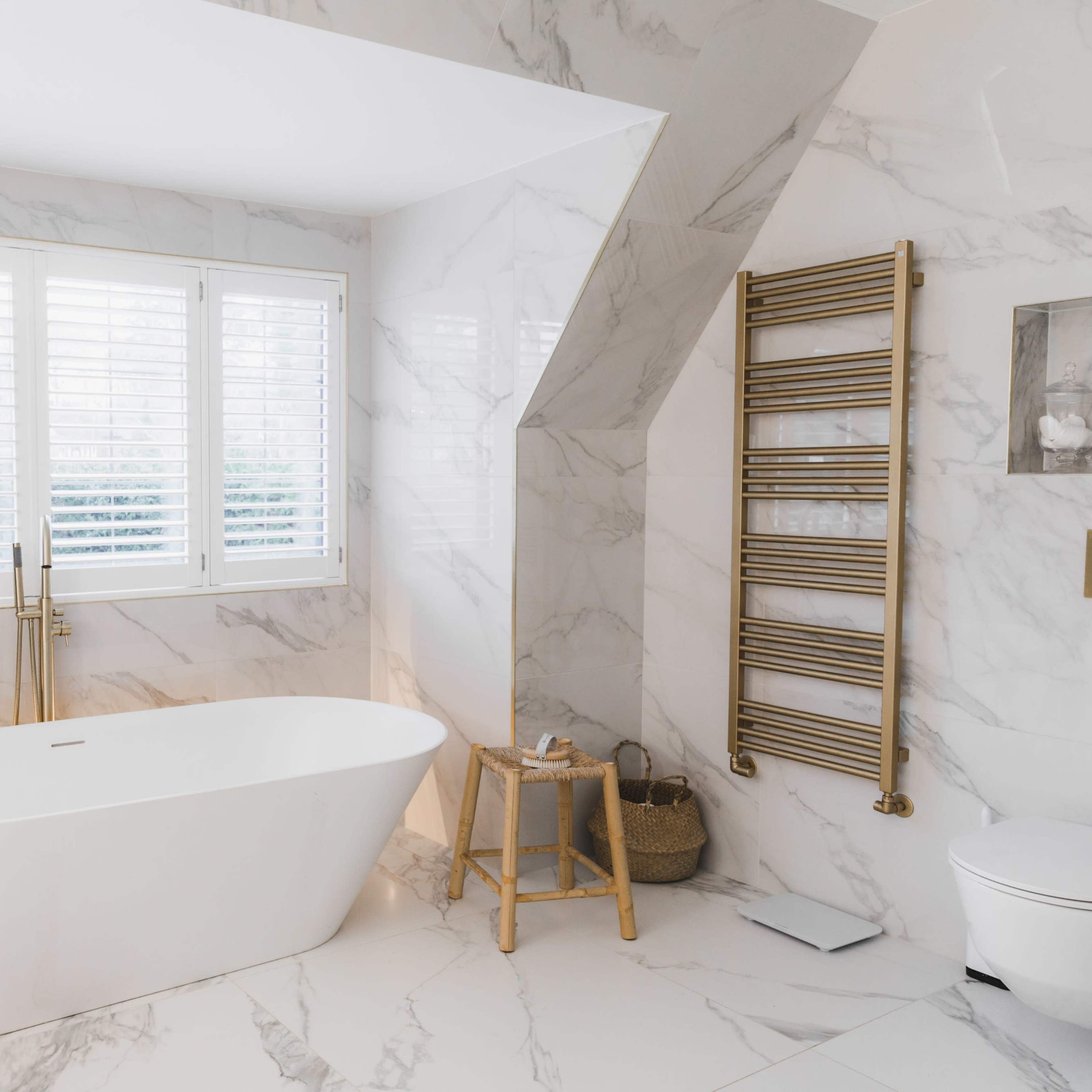 A modern bathroom features a freestanding bathtub, marble walls, and a window with shuttered blinds.