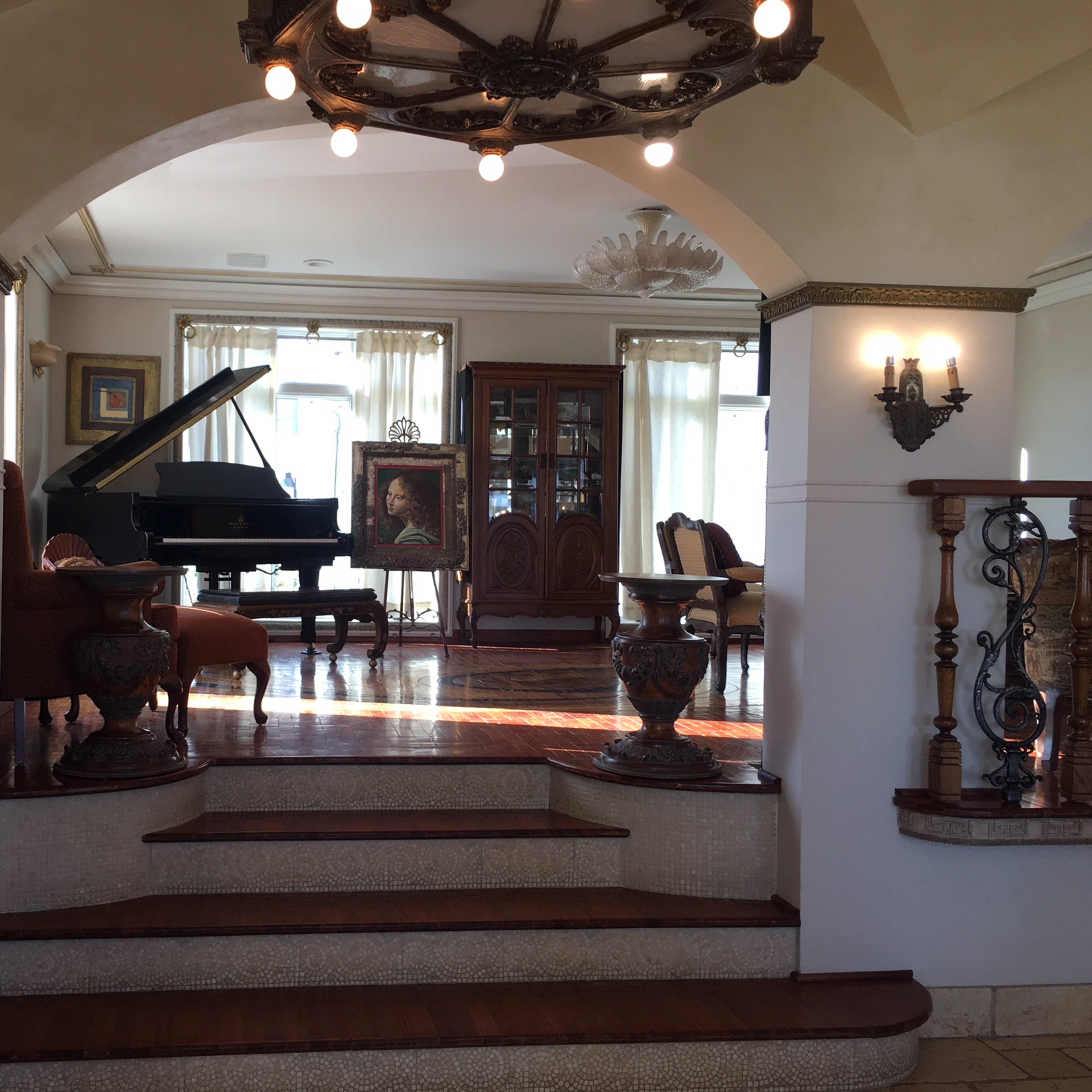A spacious living room with a grand piano, elegant furniture, and large windows allowing natural light.