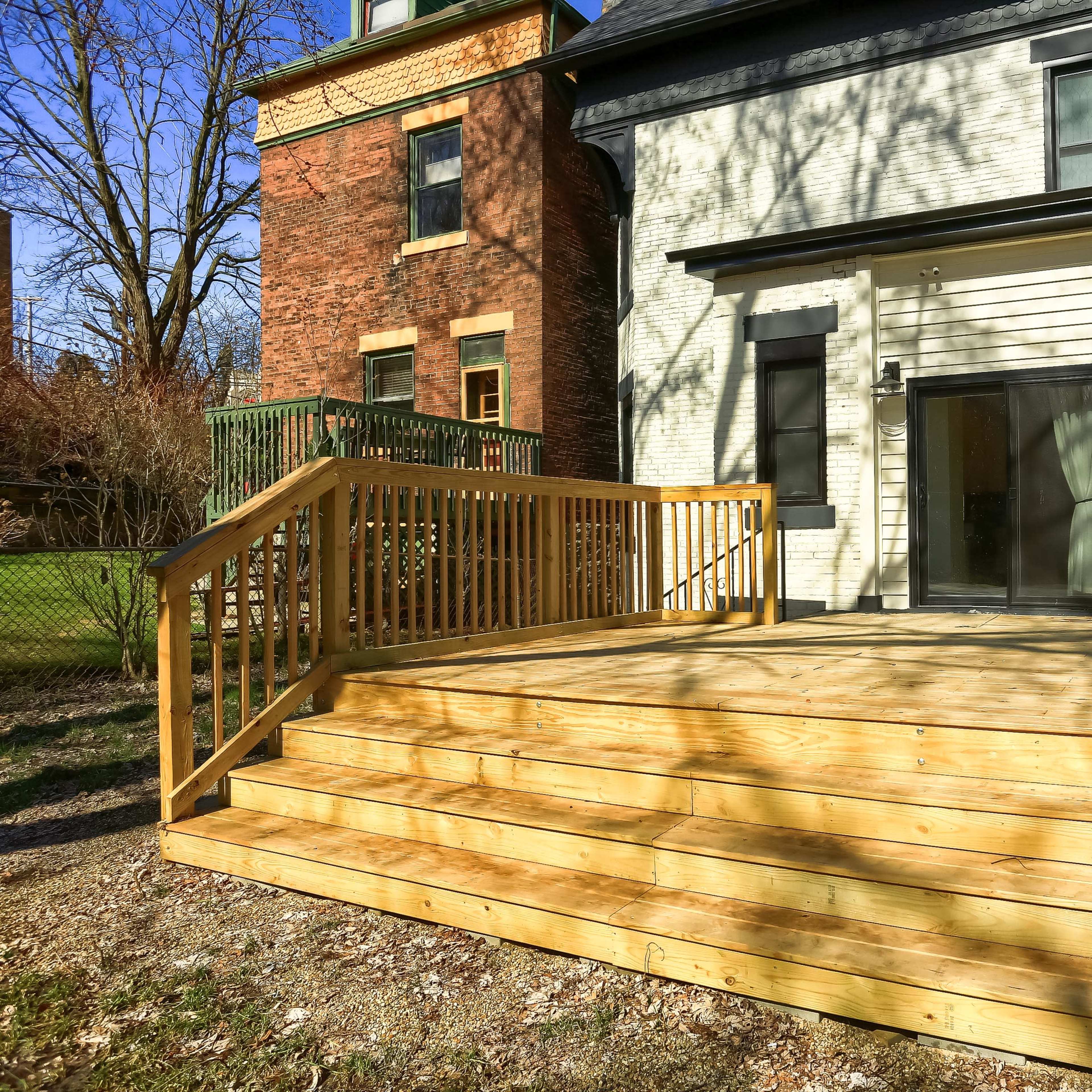 A wooden deck with a staircase, attached to the back of a two-story brick house.