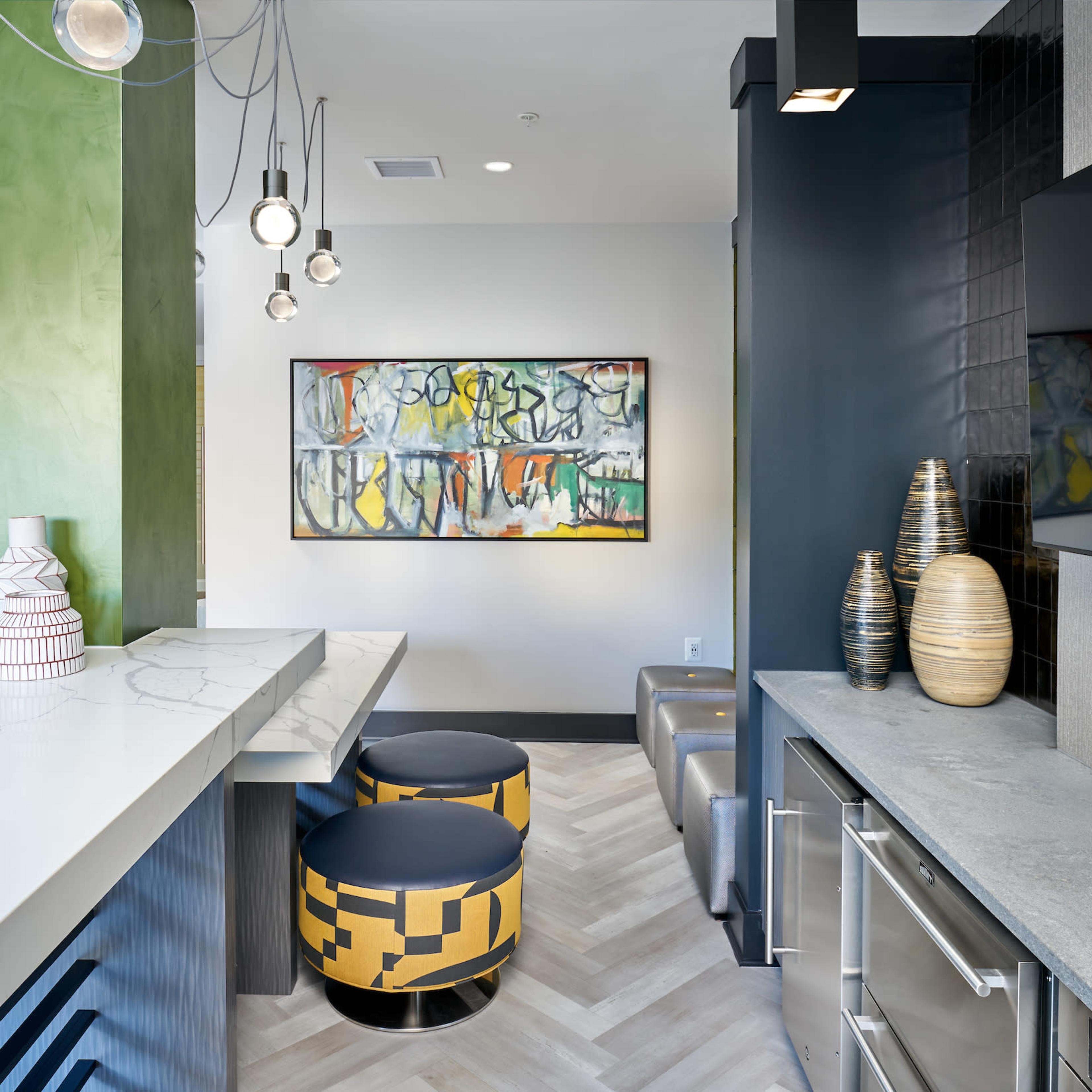 A contemporary lounge area featuring a marble countertop, colorful stools, a large abstract painting, and a mix of textured wall finishes.