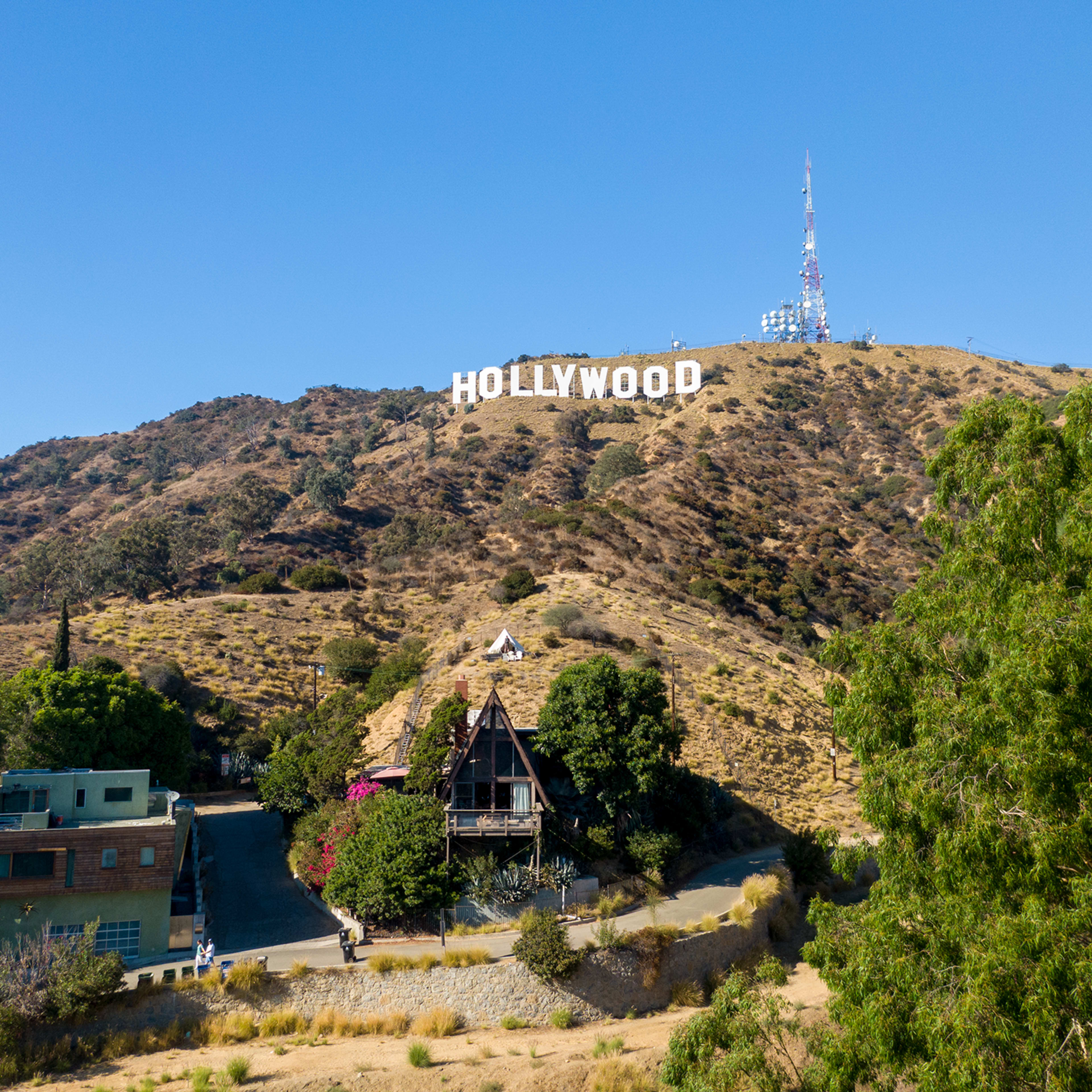 The iconic Hollywood sign is prominently displayed on a hillside, overlooking a cluster of buildings and trees below.