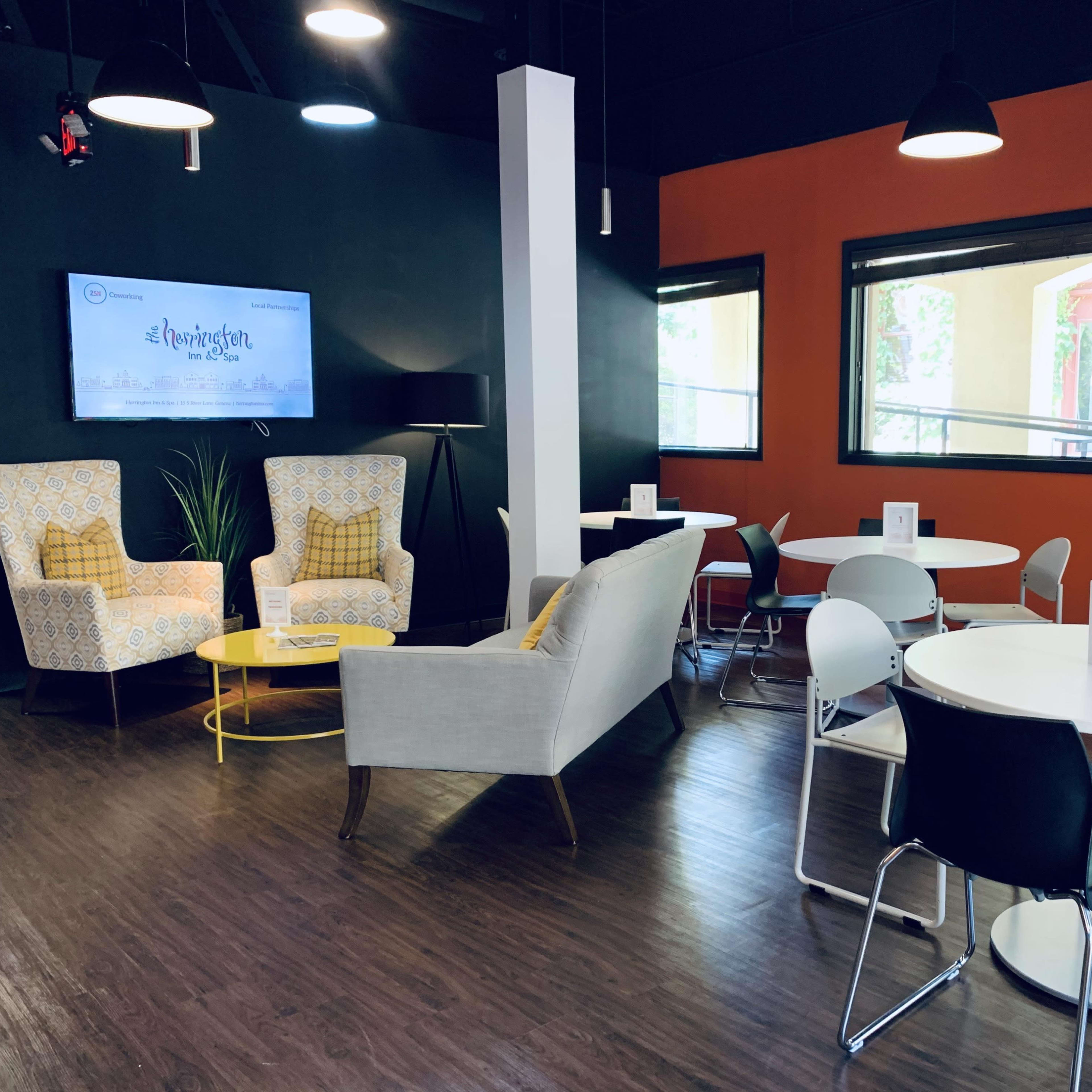 A modern lounge area with two patterned armchairs, a yellow side table, and several circular white tables with black and chrome chairs.