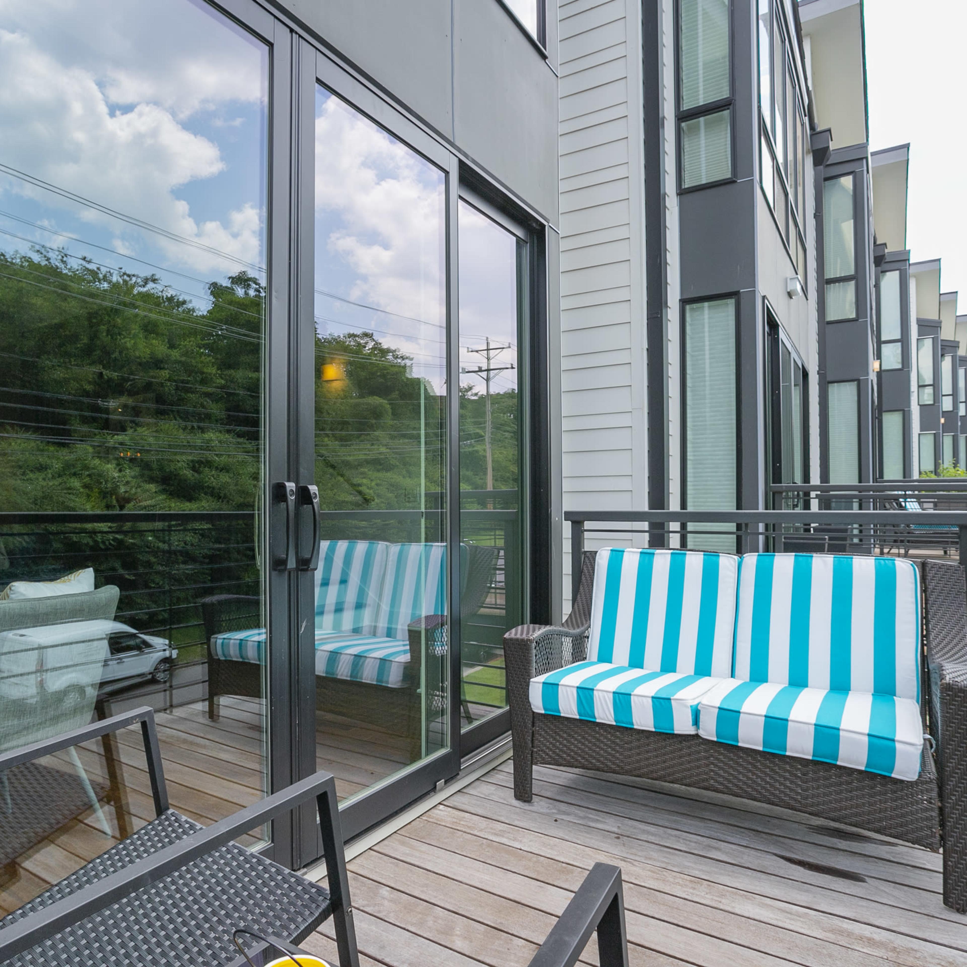 A balcony features striped seating and glass doors leading into an adjacent building.