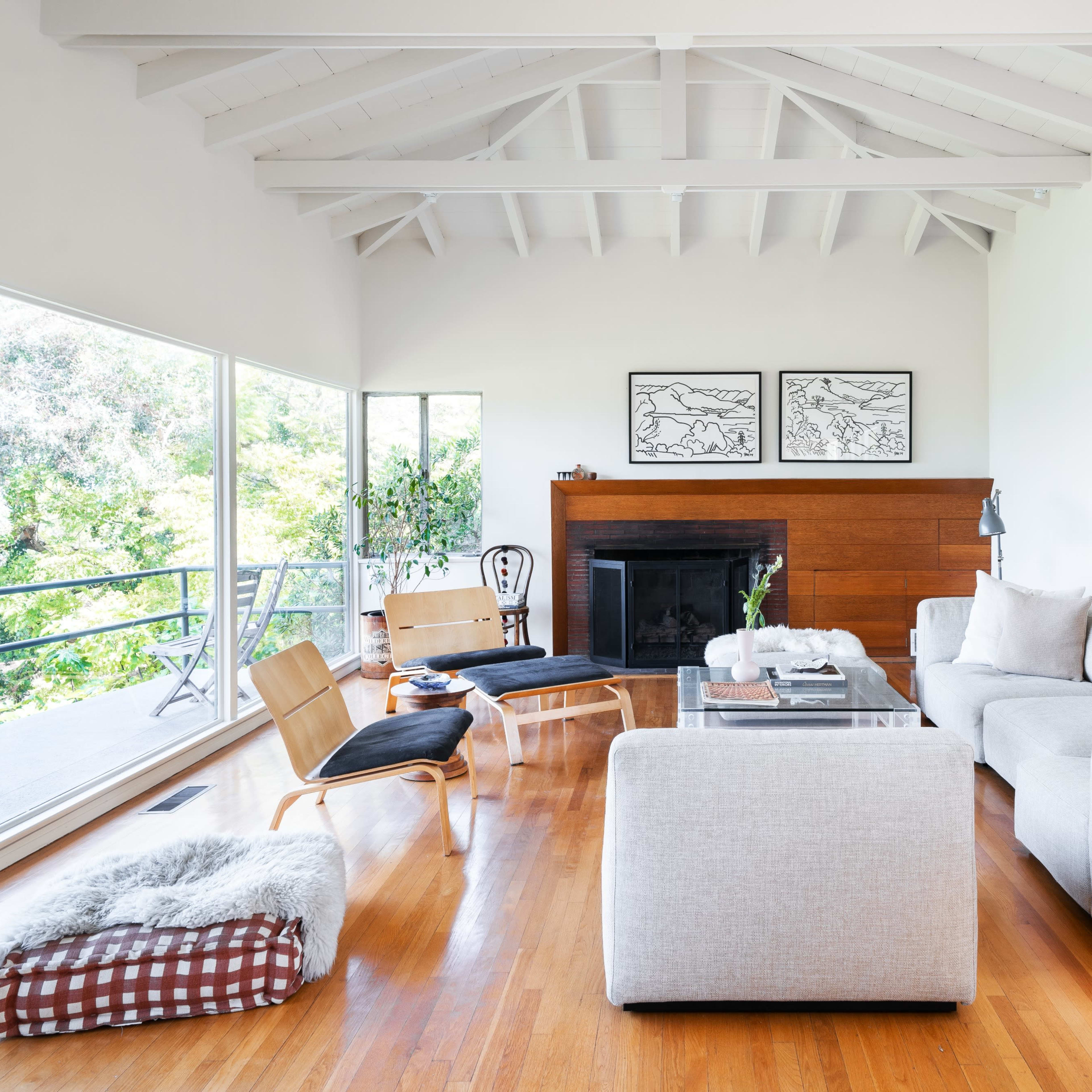 A bright living room features a large sectional sofa, a wooden coffee table, and art on the walls, with large windows offering views of the outdoors.