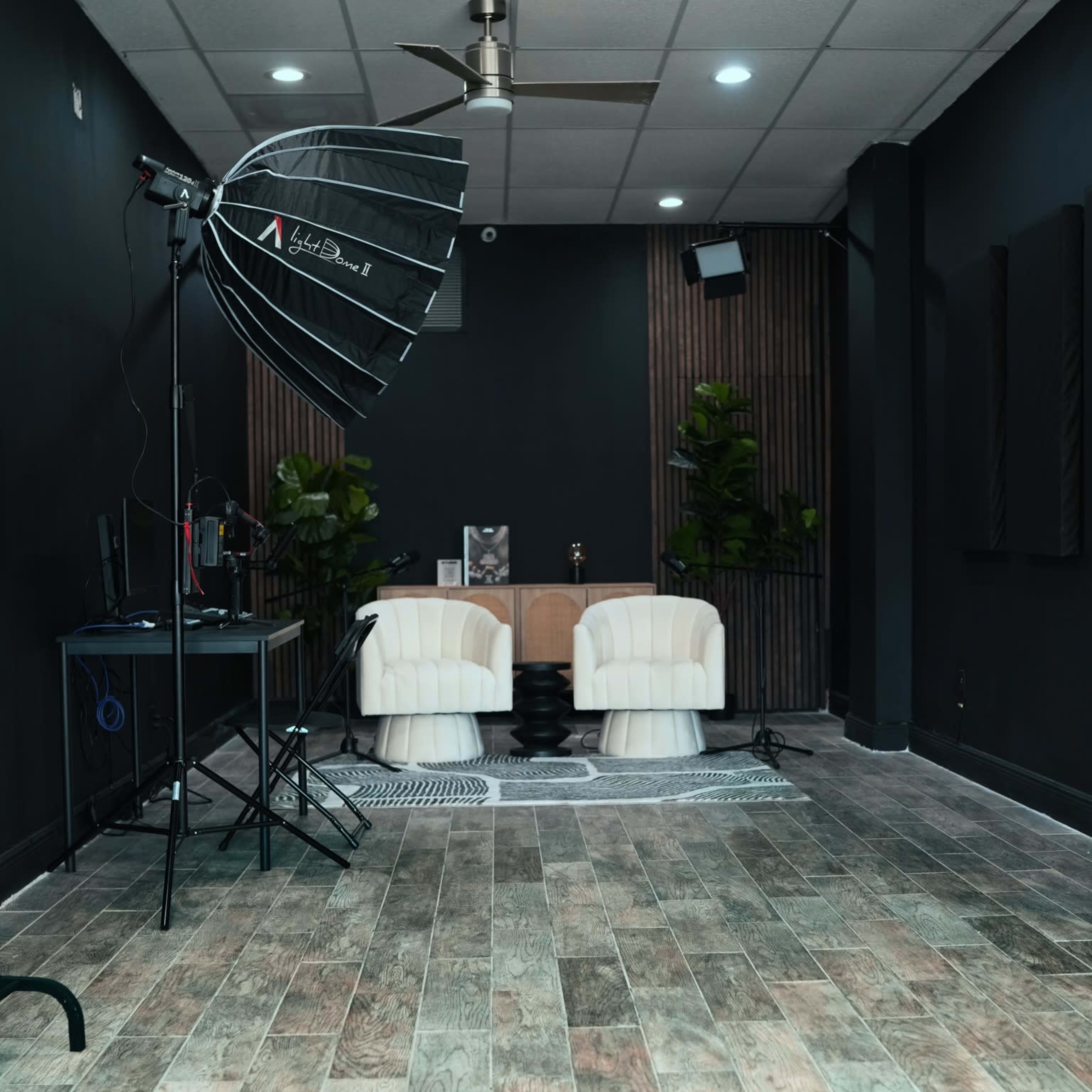 A photography studio featuring two white chairs, a backdrop, and studio lighting equipment against a dark wall.