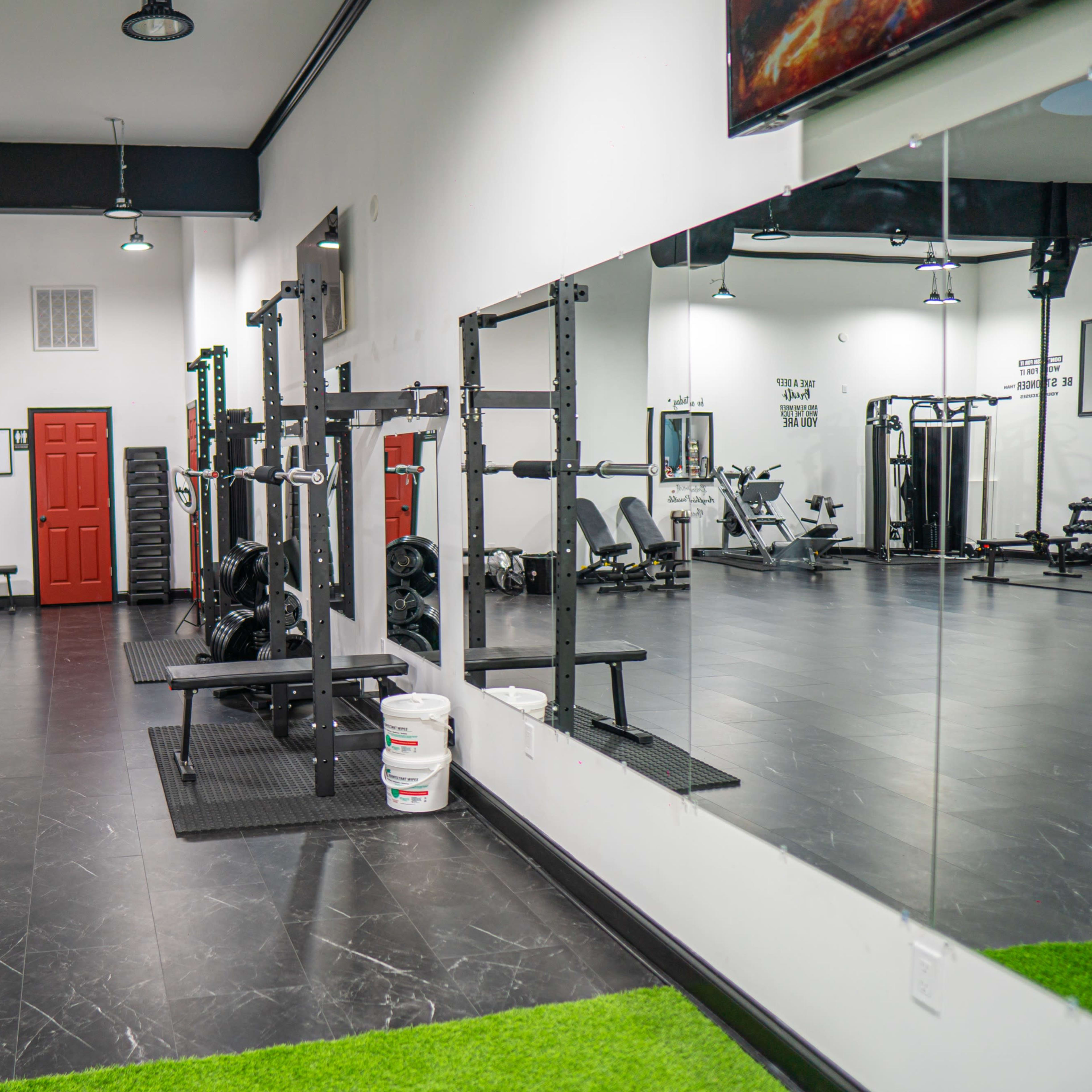 A modern gym interior featuring weightlifting equipment and exercise machines arranged around a mirrored wall.