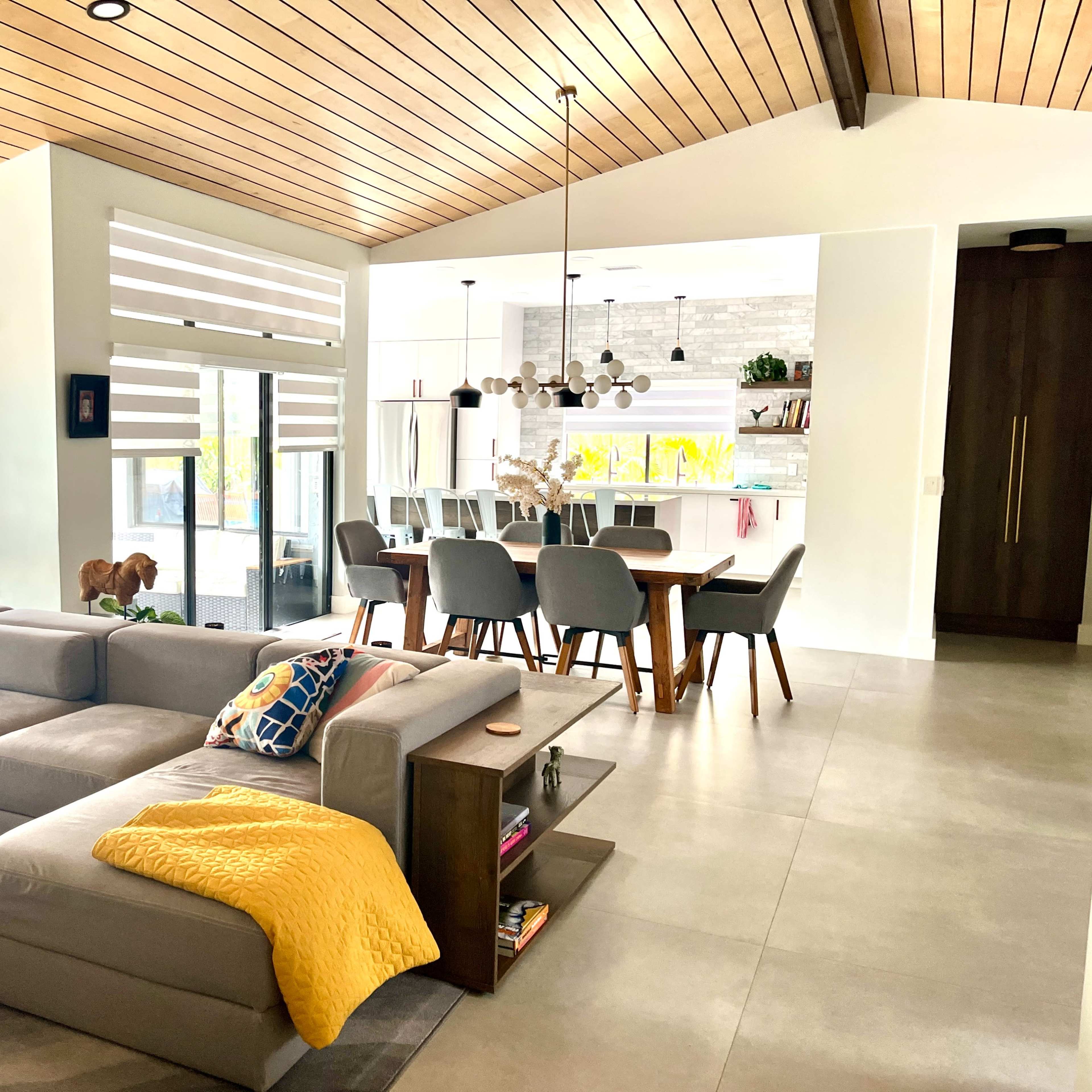 A modern living space featuring a sectional sofa, dining area, and a kitchen with contemporary furnishings and large windows.