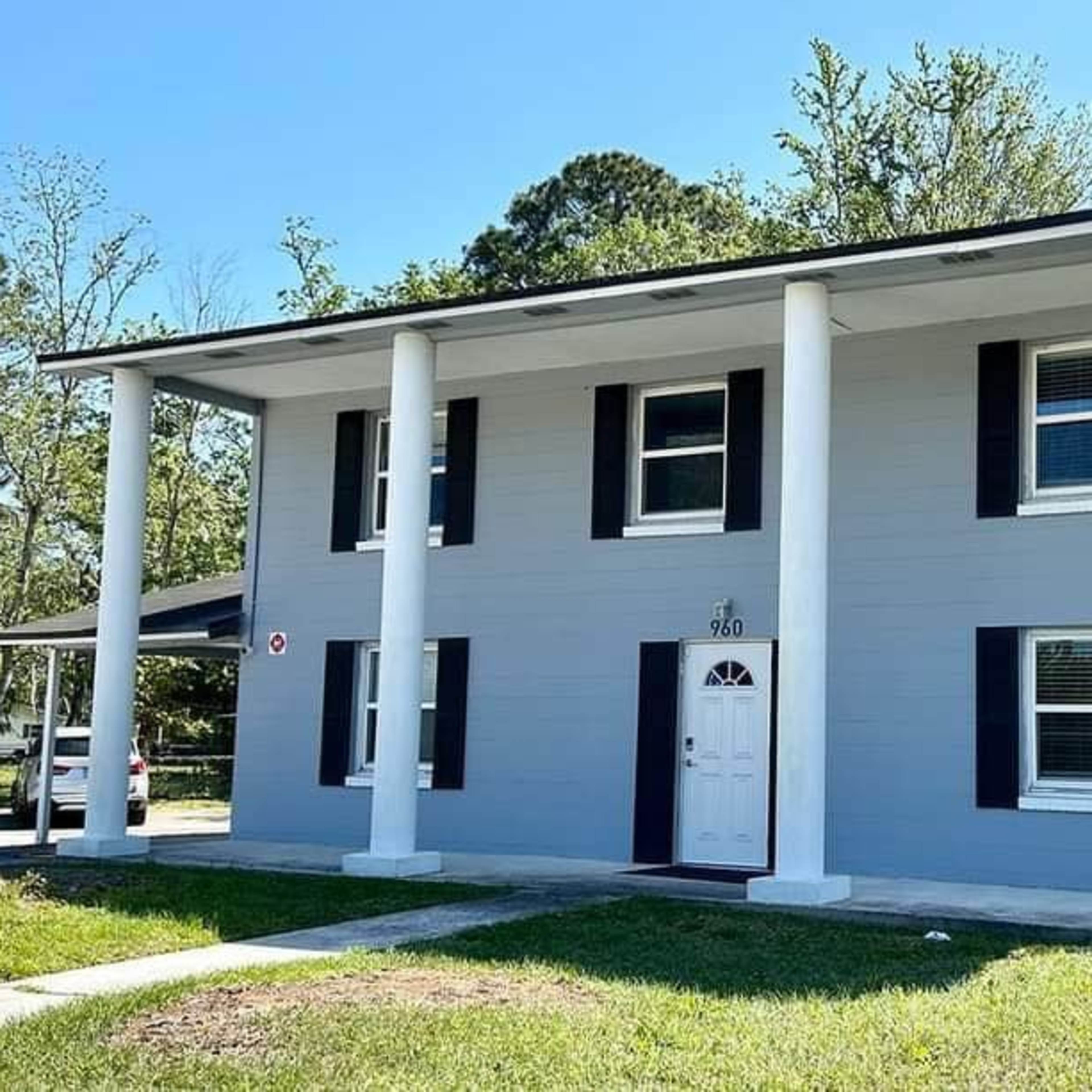 A two-story house with four windows, a front door, and white columns on either side of the entrance.