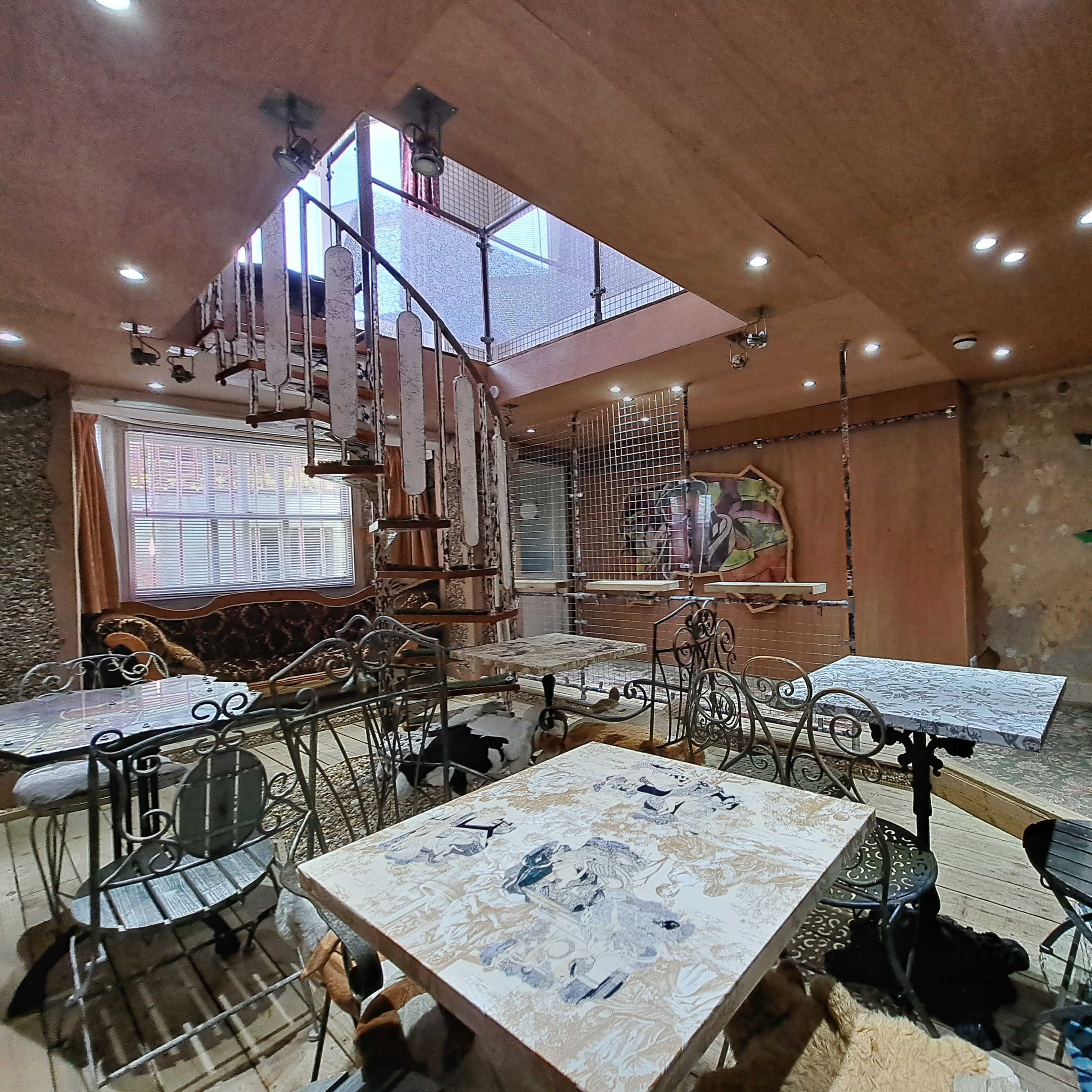 A multi-level room with a spiral staircase, various tables, and walls displaying an eclectic mix of decor and photographs.