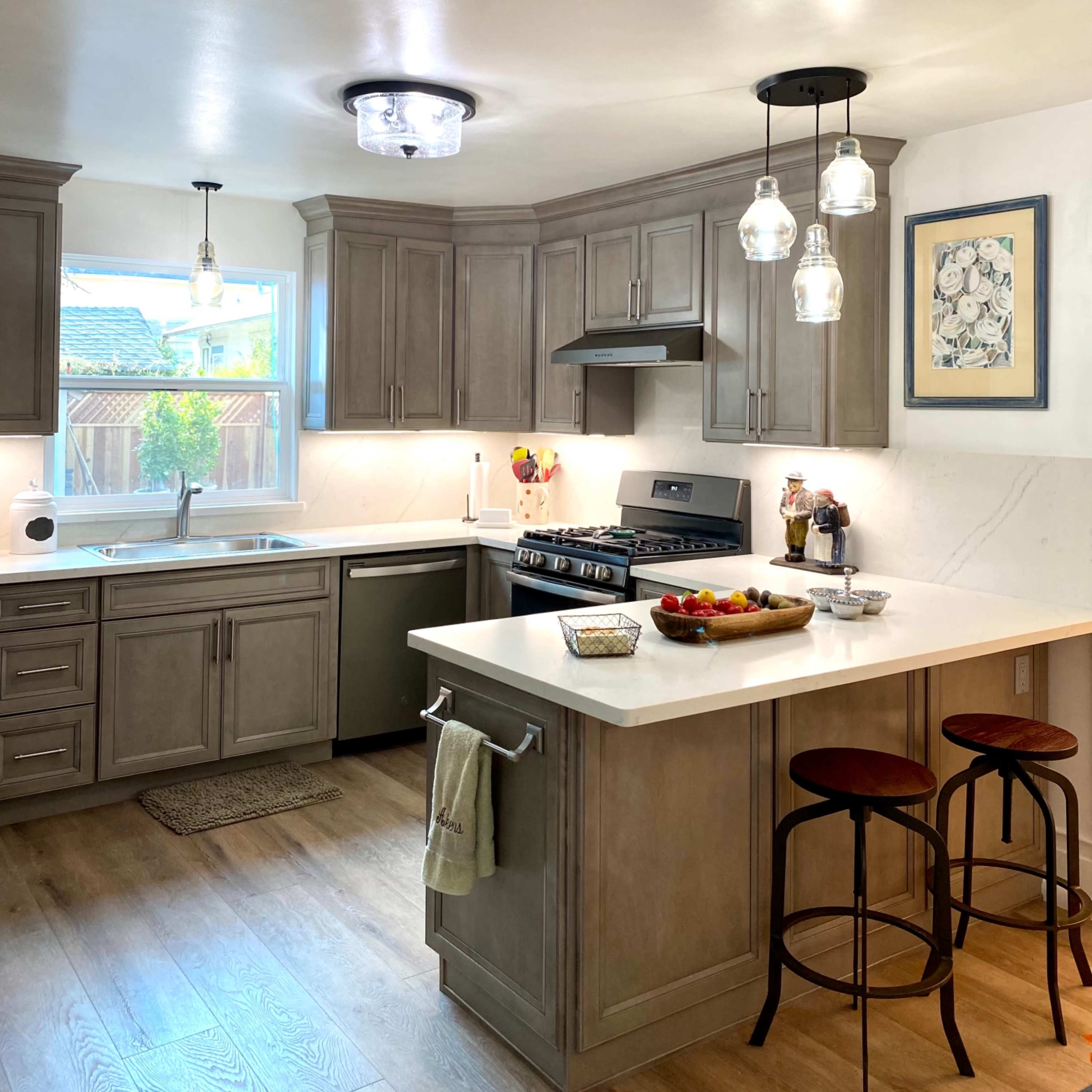 A modern kitchen features gray cabinetry, a central island with bar stools, and pendant lighting above the countertop.