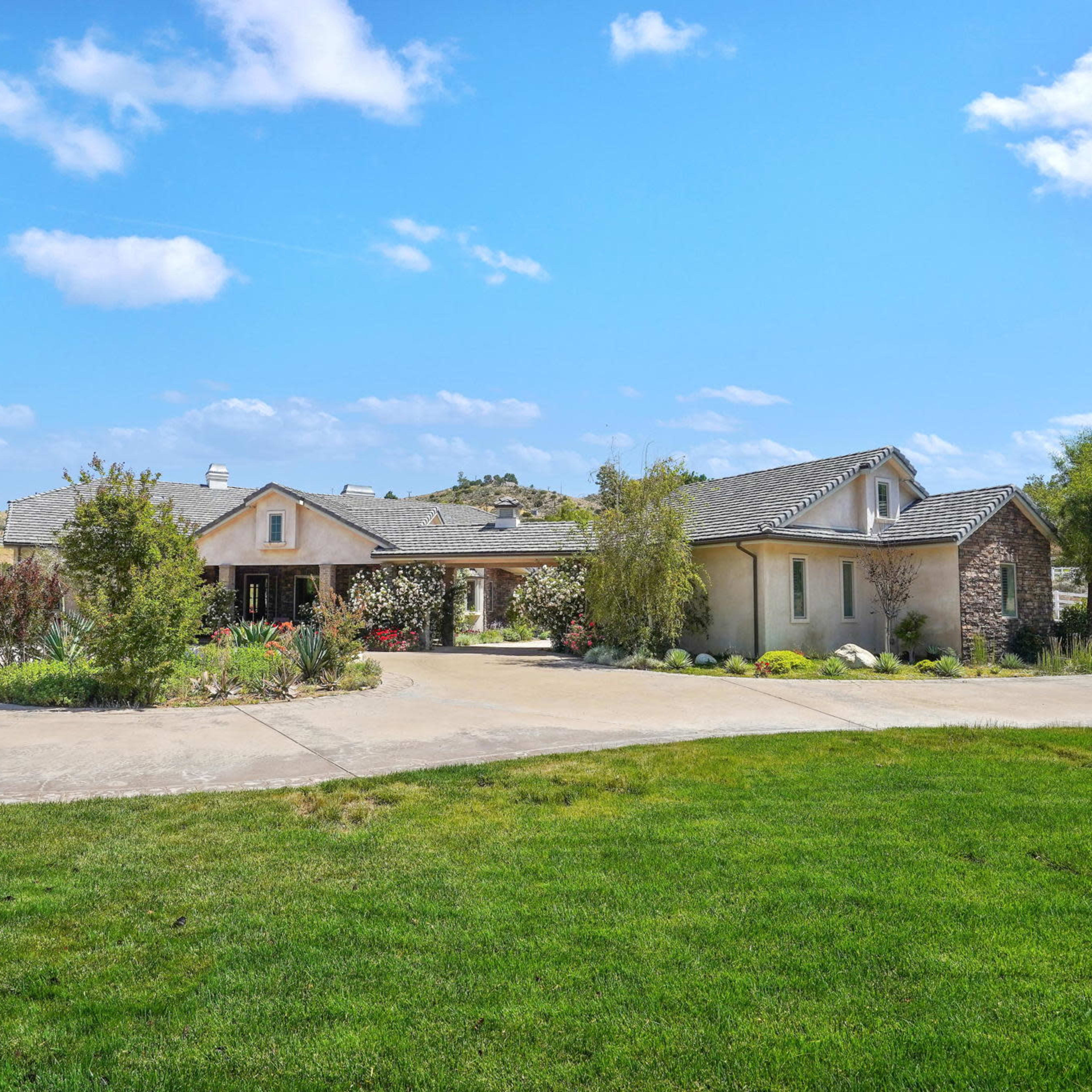 A single-story house with a stone accent and a landscaped front yard is set against a blue sky with scattered clouds.