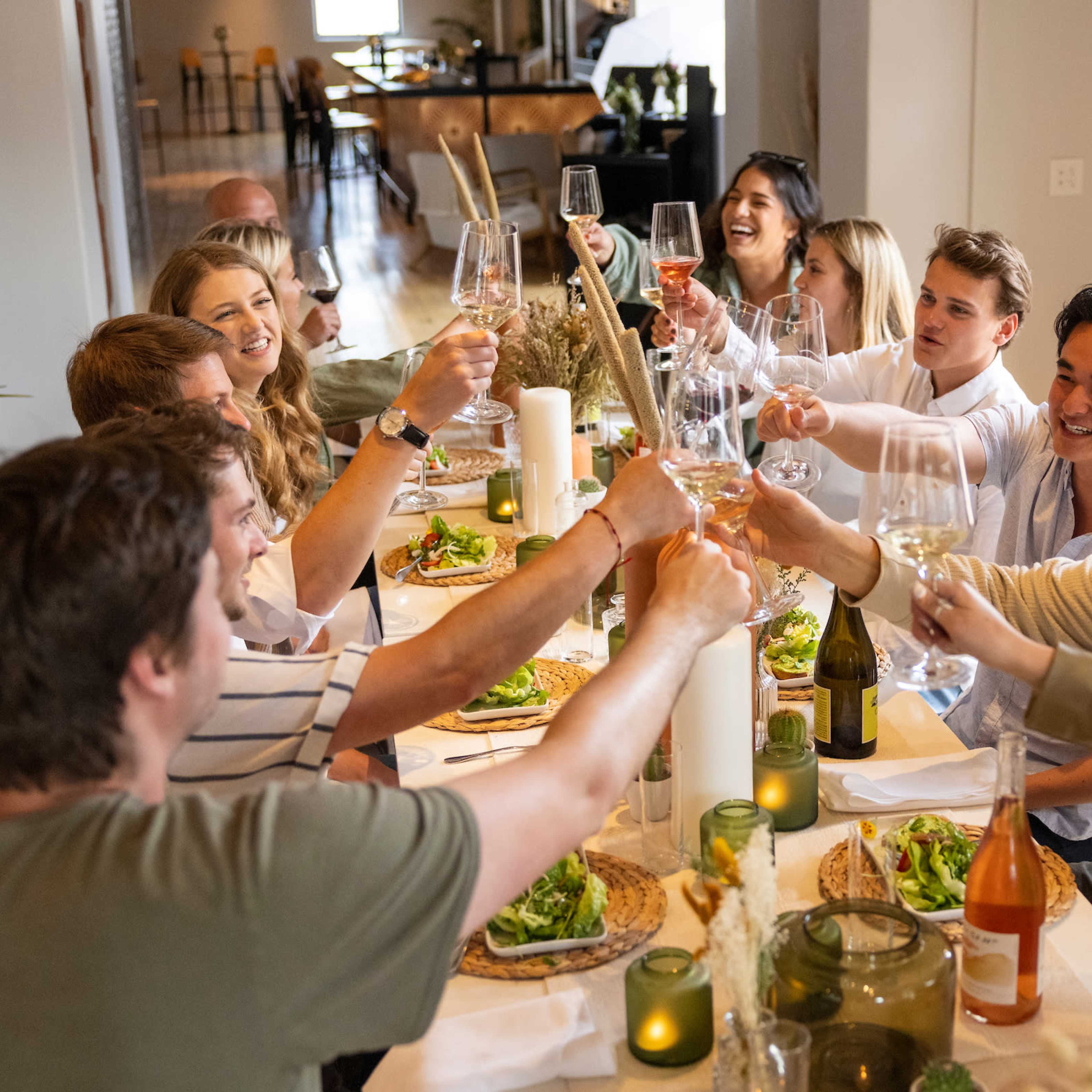 A group of people is gathered around a dining table, raising their glasses in a toast while enjoying a meal.