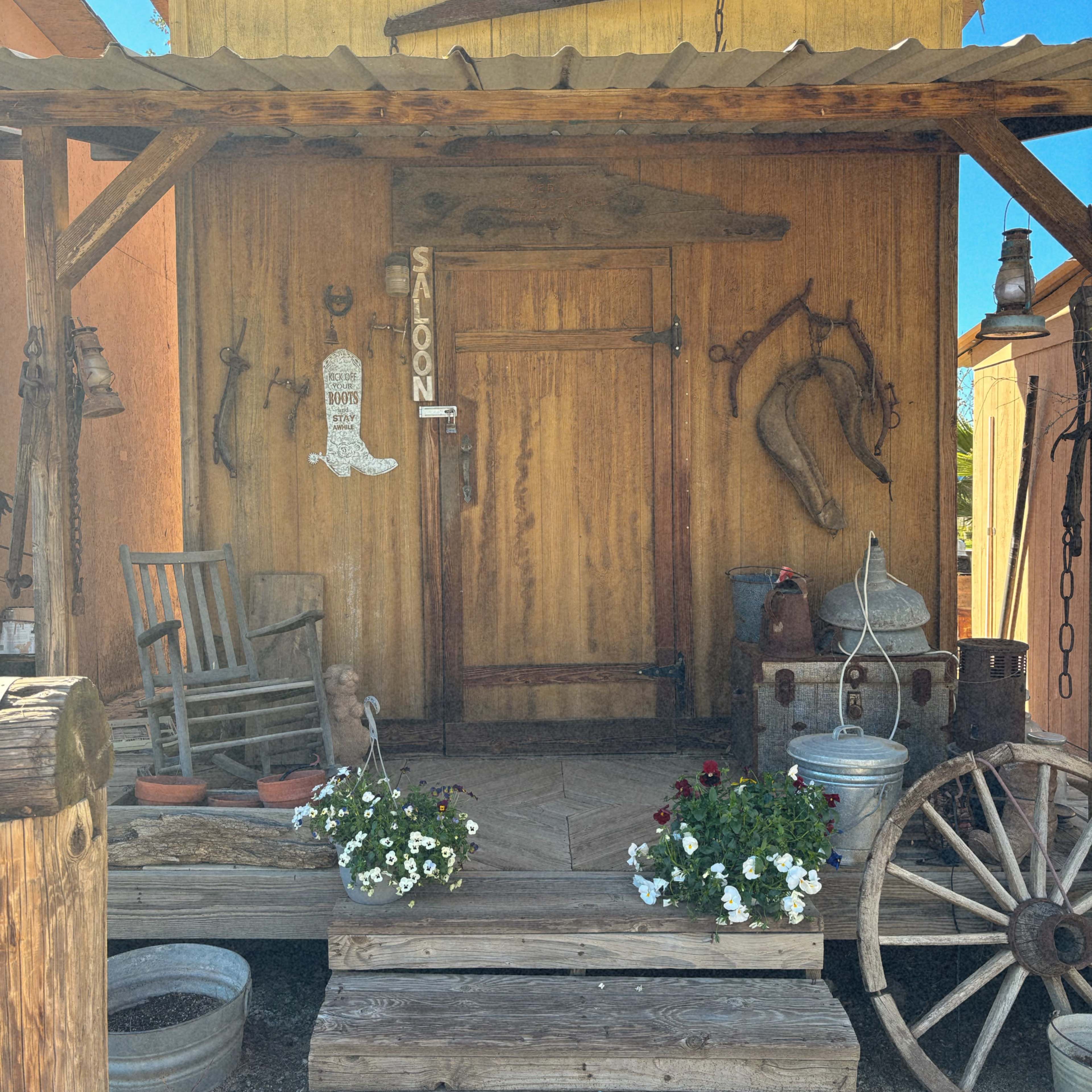 A wooden saloon front with a rocking chair, decorative horseshoes, and flower pots on the porch steps.