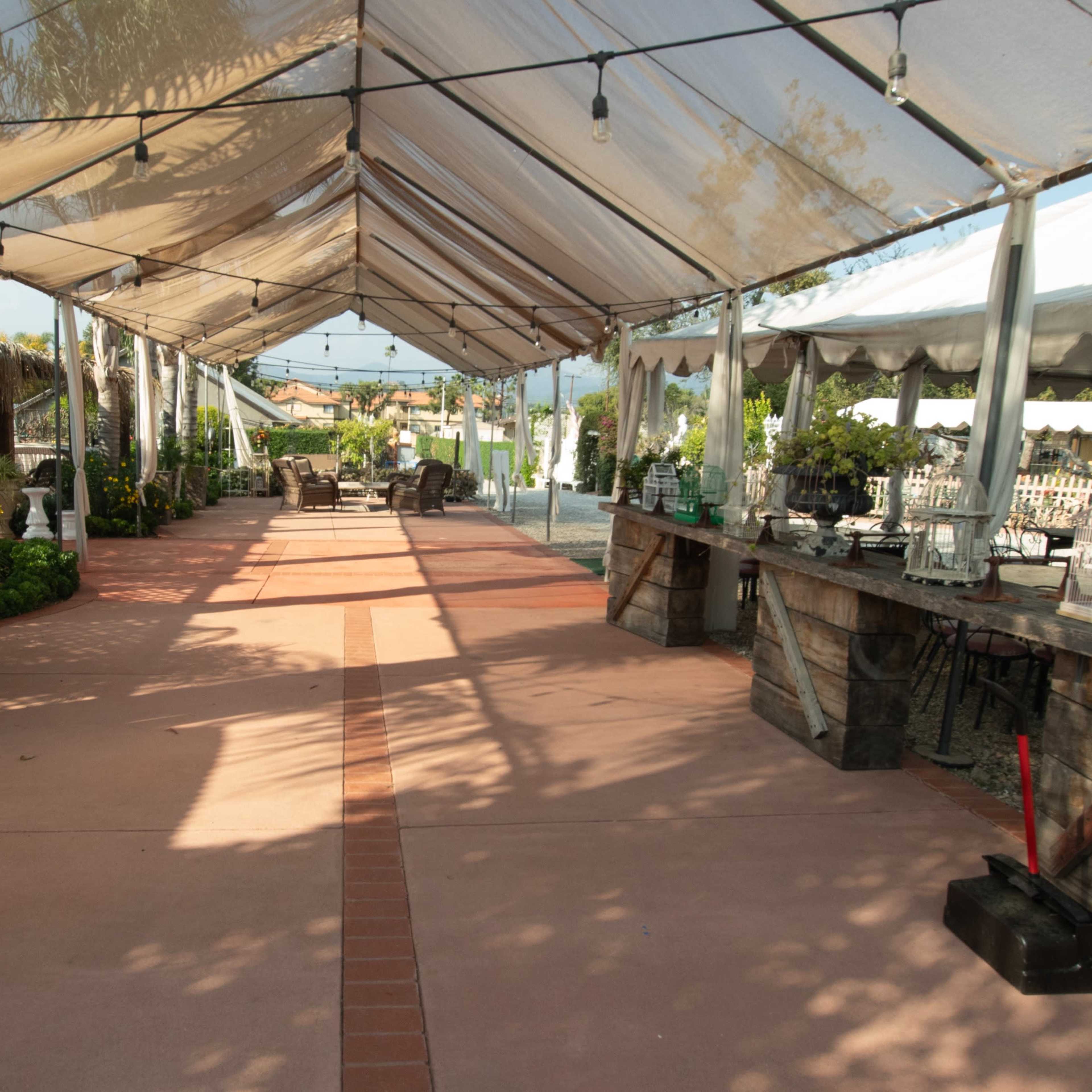 A spacious outdoor venue with a covered walkway lined with plants and a bar area on one side.