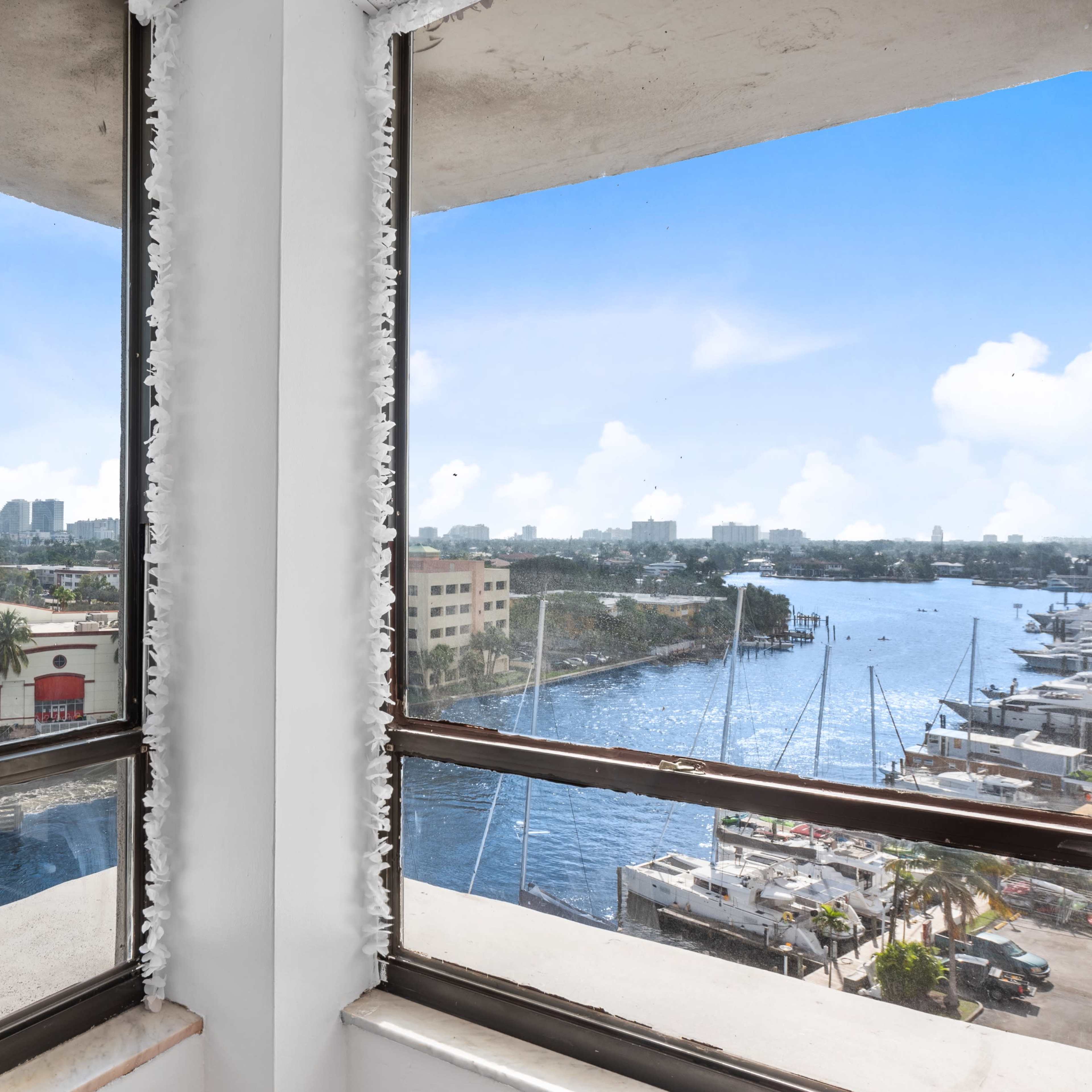 A view from a corner window overlooking a marina and cityscape with palm trees and buildings in the distance.