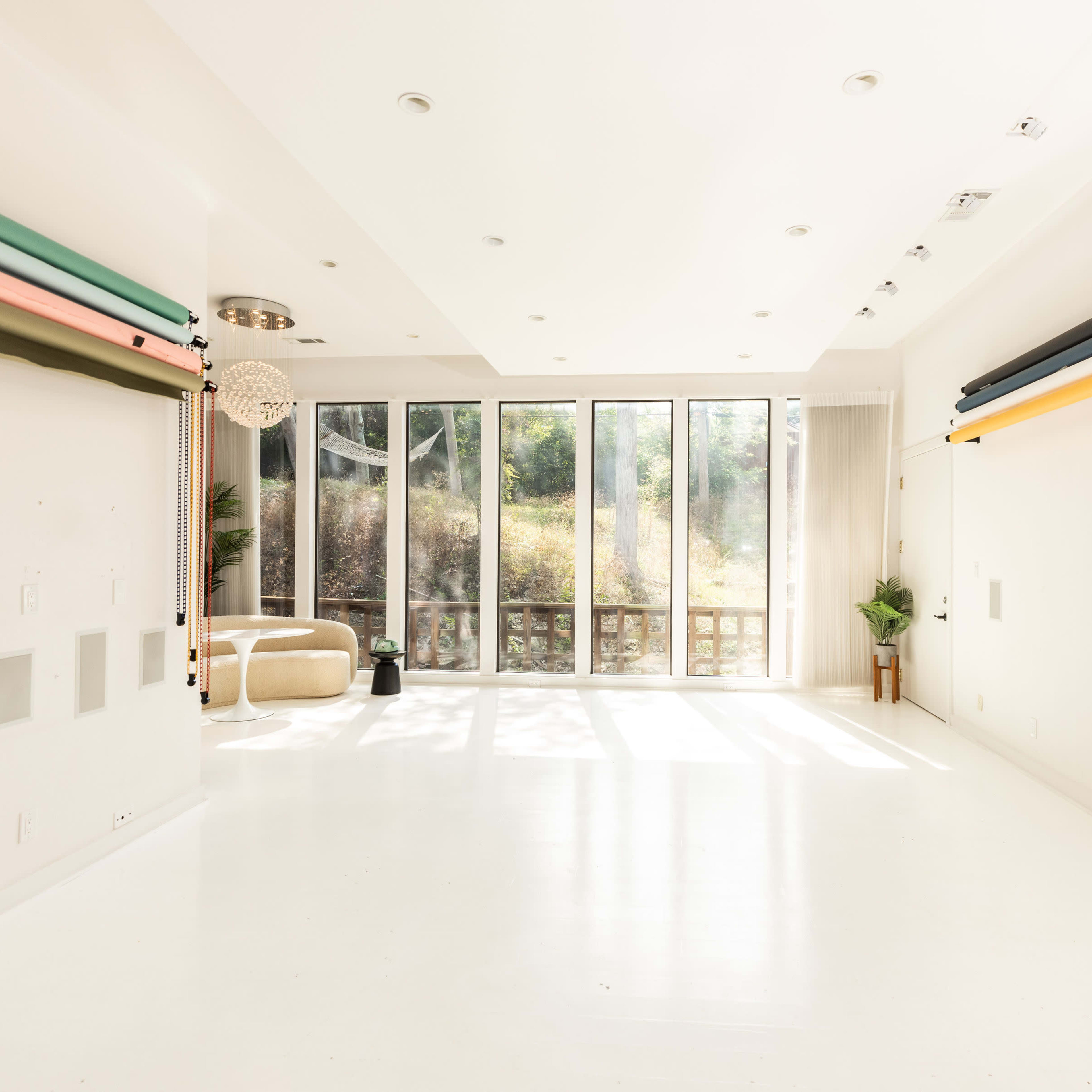 A bright, minimalist room with large windows, featuring colorful resistance bands mounted on the walls and a simple seating area.