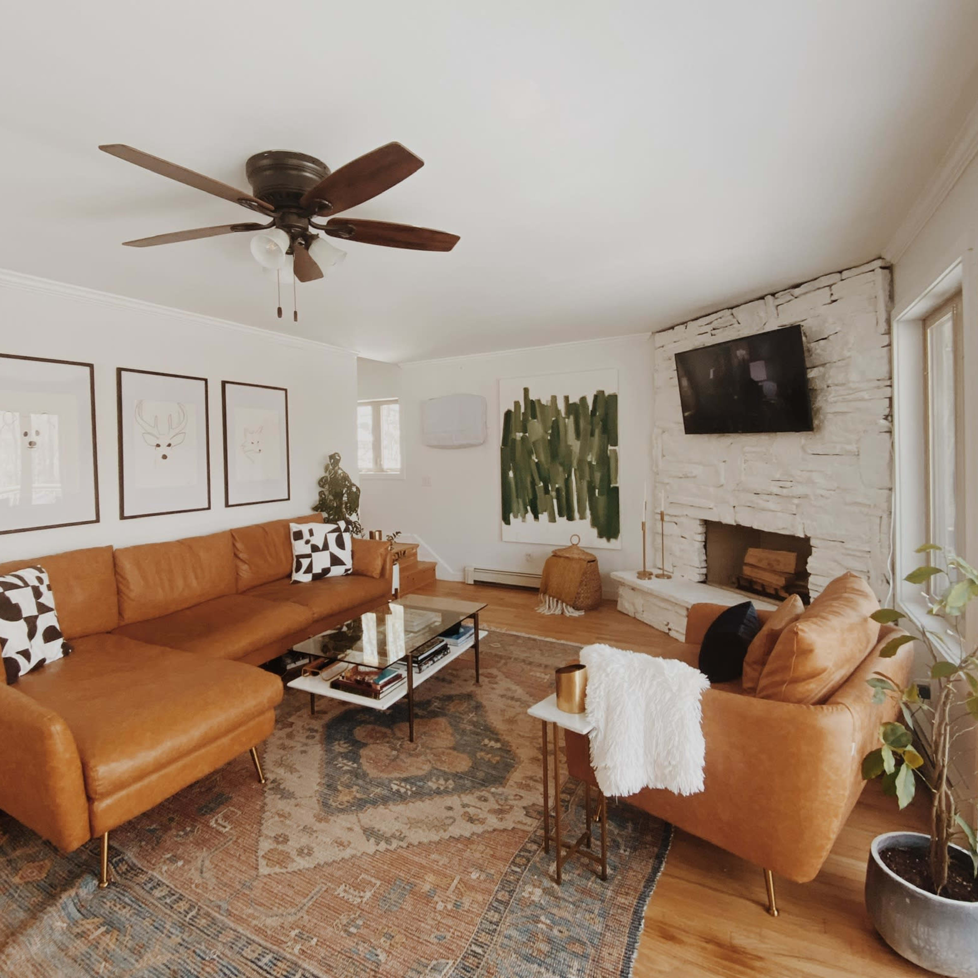 A spacious living room features a large brown sectional sofa, a coffee table, and a stone fireplace, complemented by wall art and large windows.