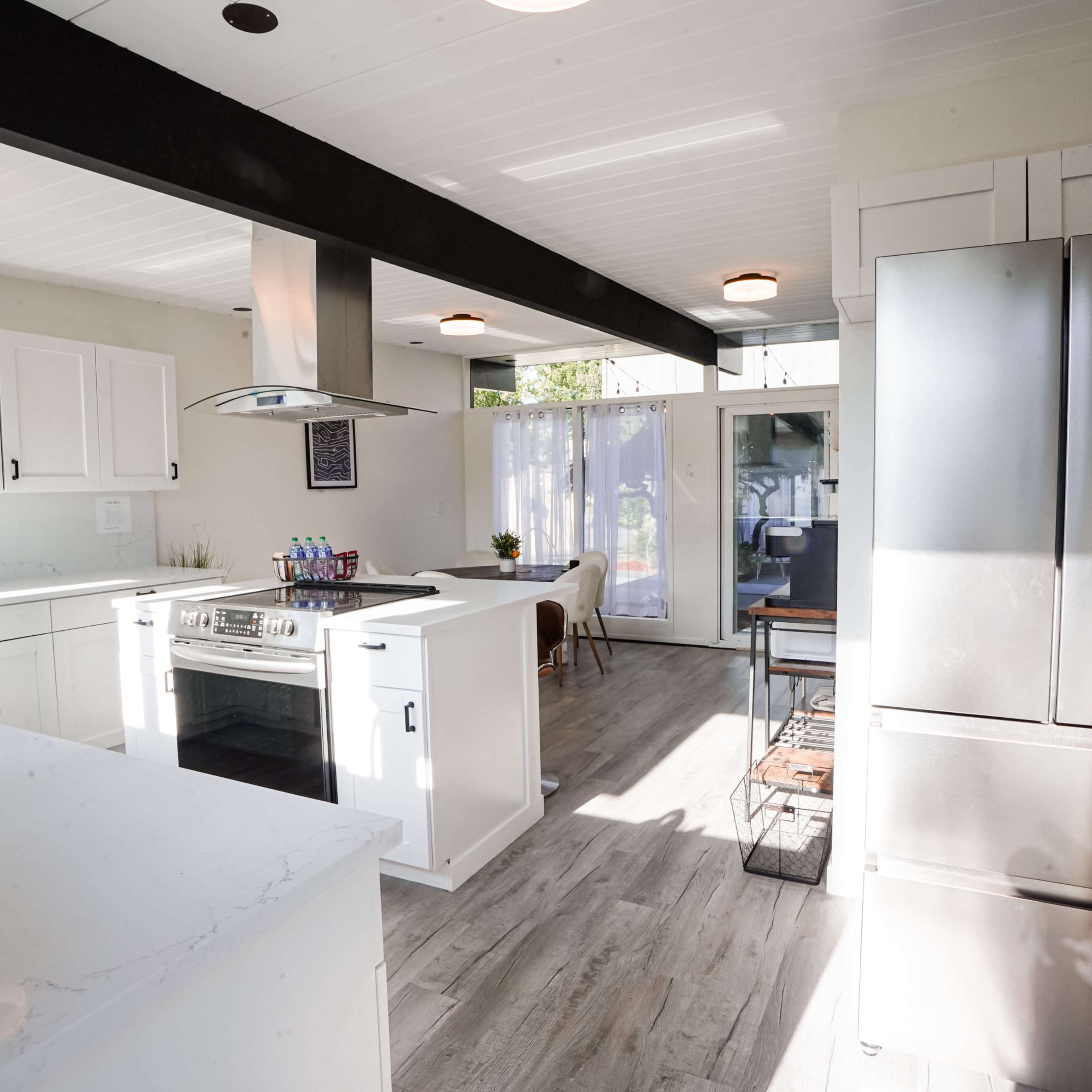 A modern kitchen with white cabinets, a central island with a stove, and stainless steel appliances, including a refrigerator.