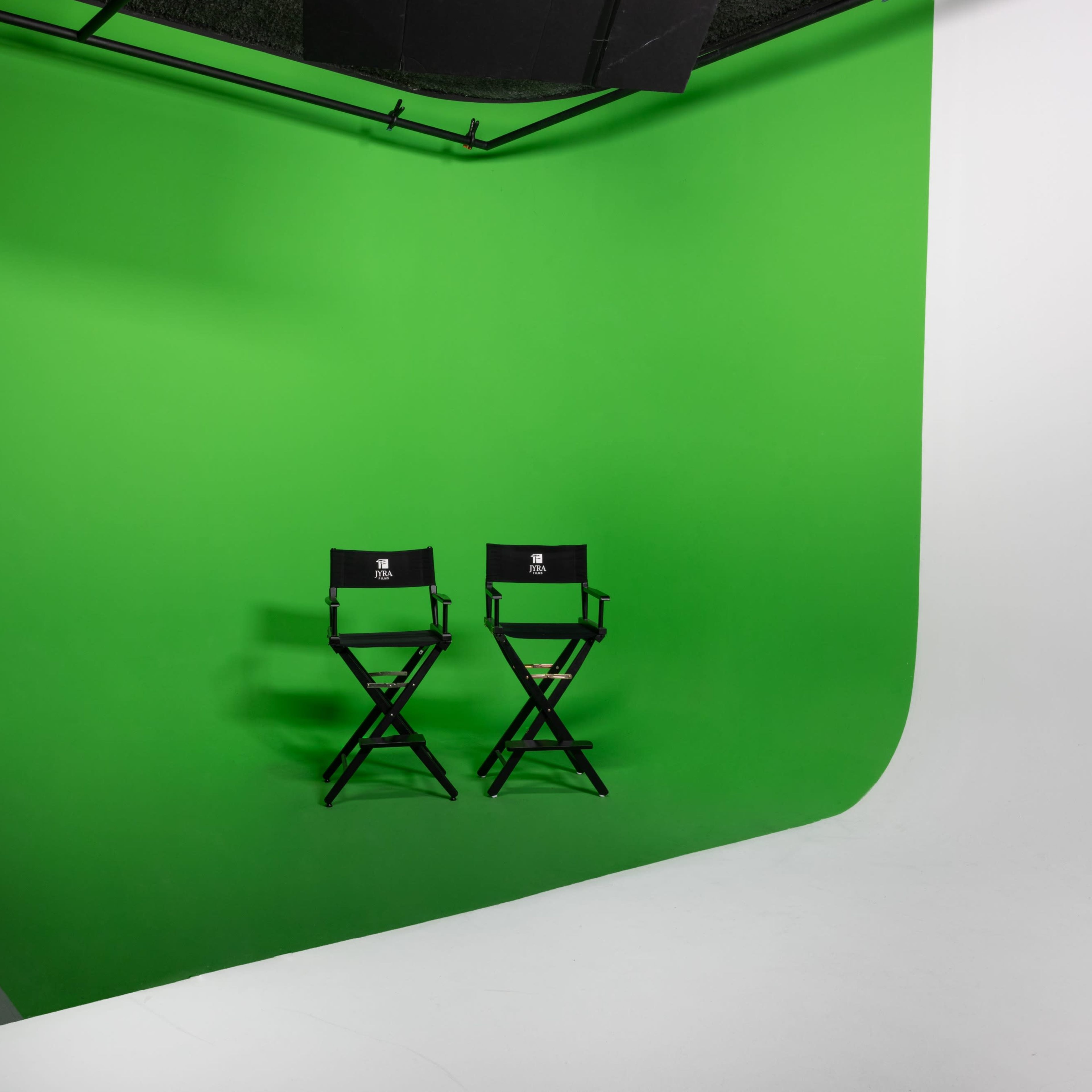 Two black director's chairs positioned in front of a bright green backdrop in a studio setting.