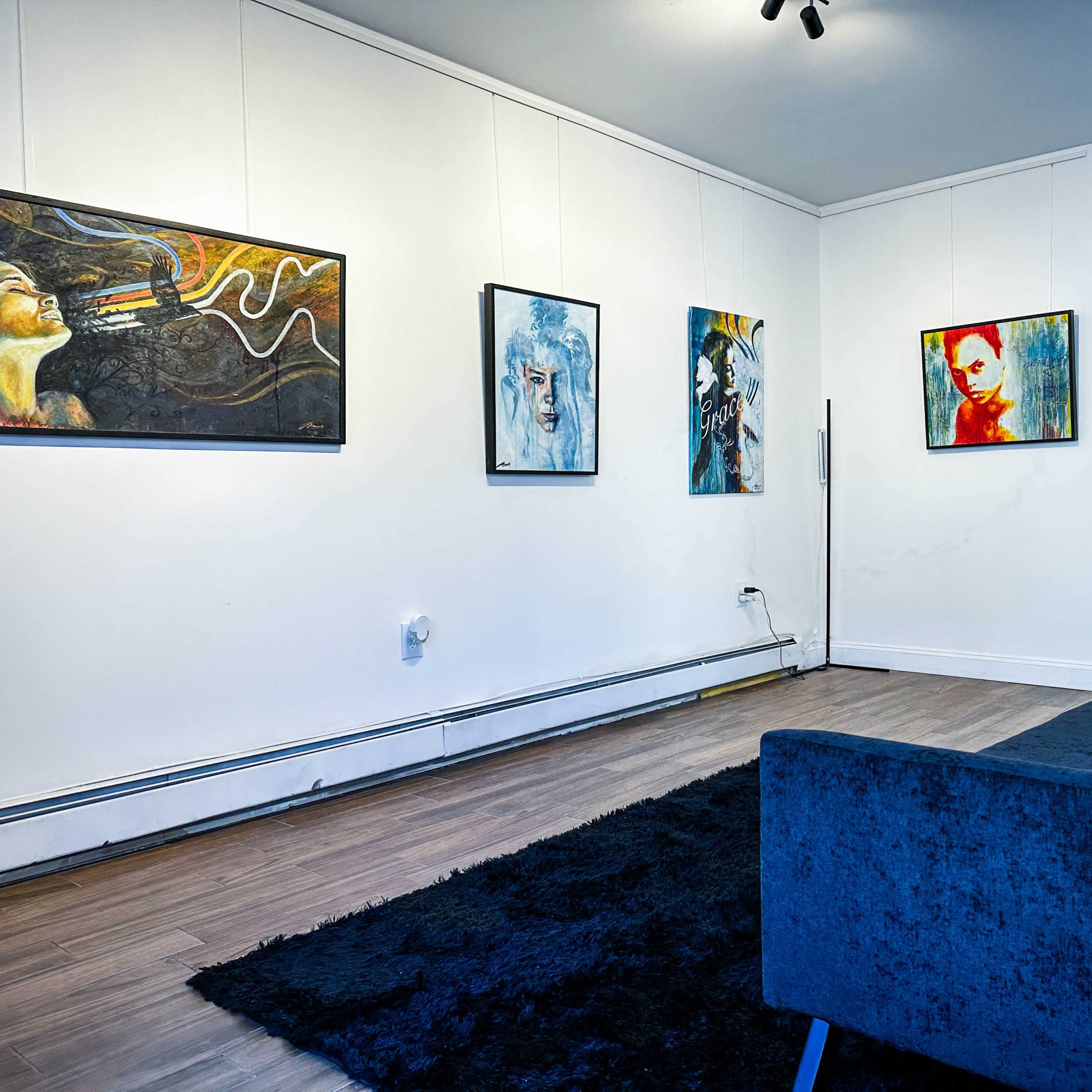 A gallery wall featuring several framed paintings, with a dark sofa placed on a textured rug in the foreground.
