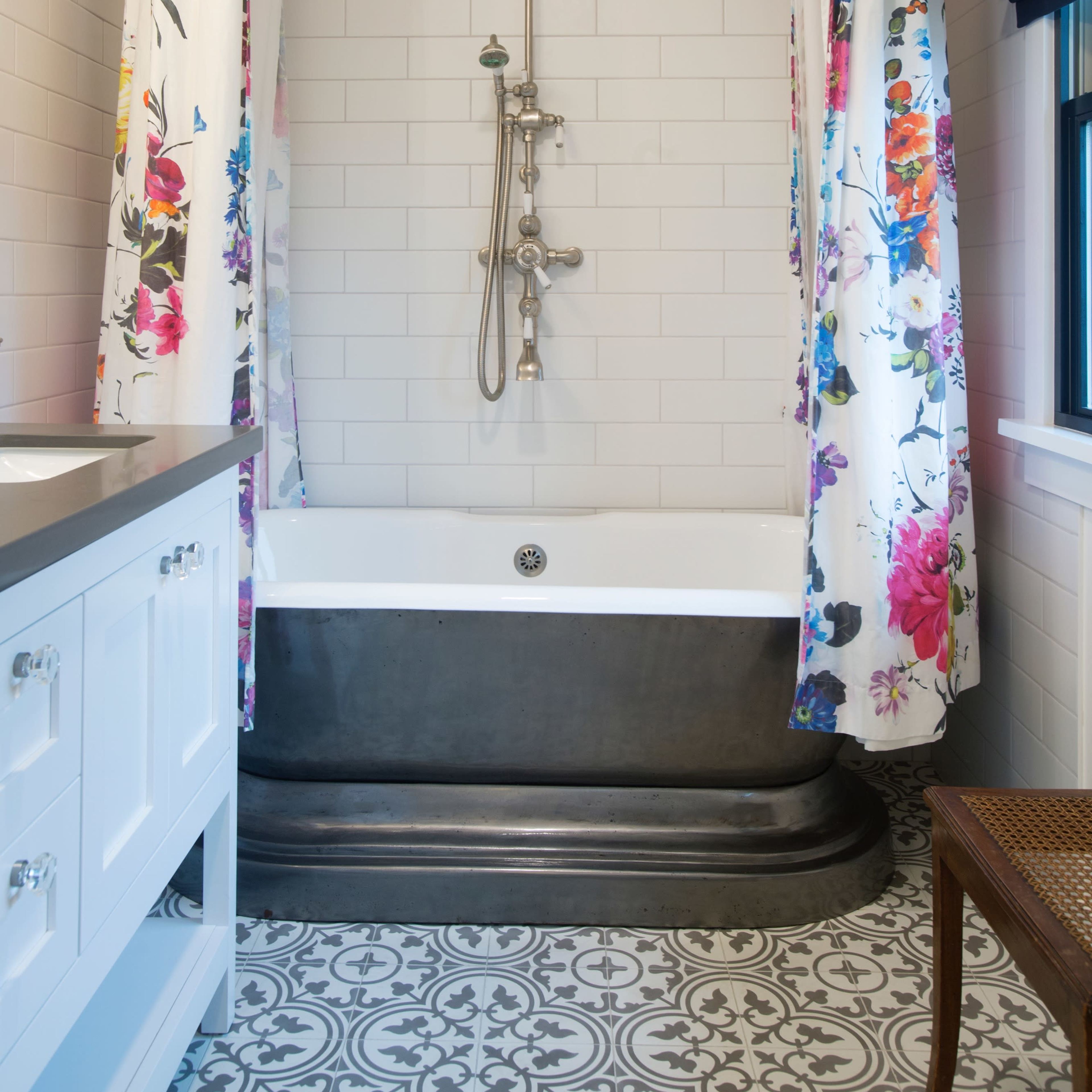 A bathroom with a shower and bathtub combination, featuring floral-patterned curtains and a patterned tile floor.