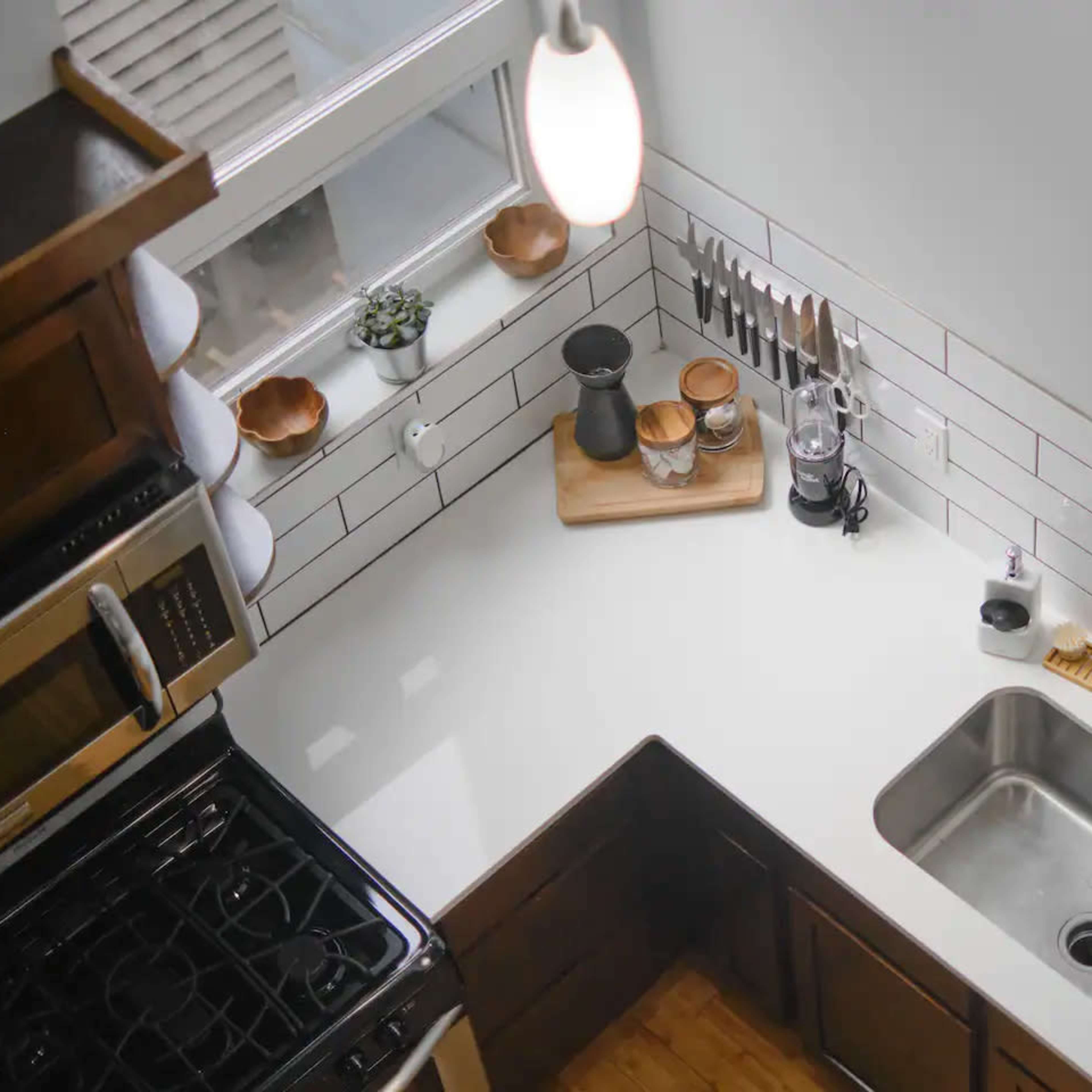 A modern kitchen with an L-shaped counter featuring a stainless steel sink, cooking utensils, and a window overhead.