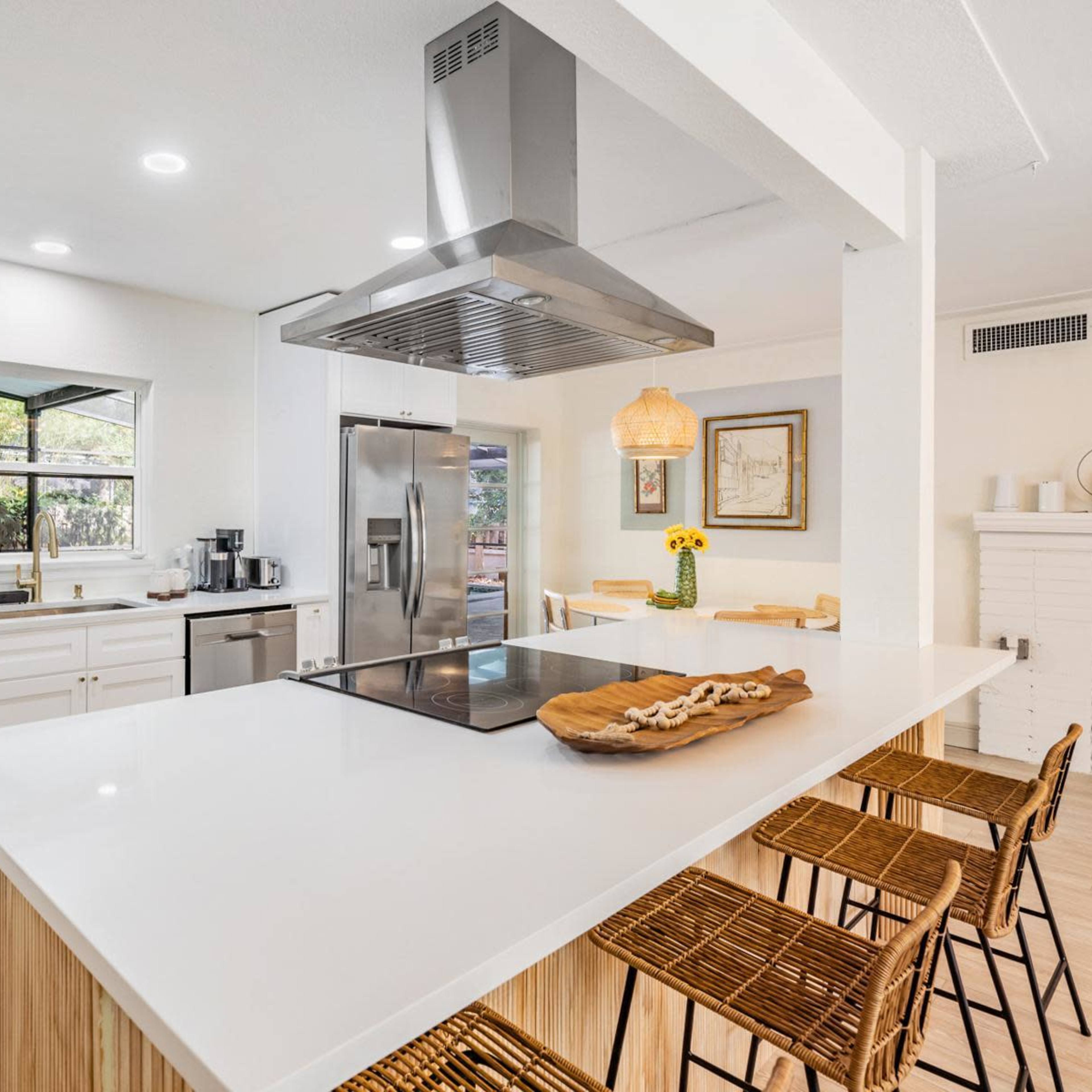A modern kitchen features white cabinetry, a large island with an integrated cooktop, and a stainless steel refrigerator.