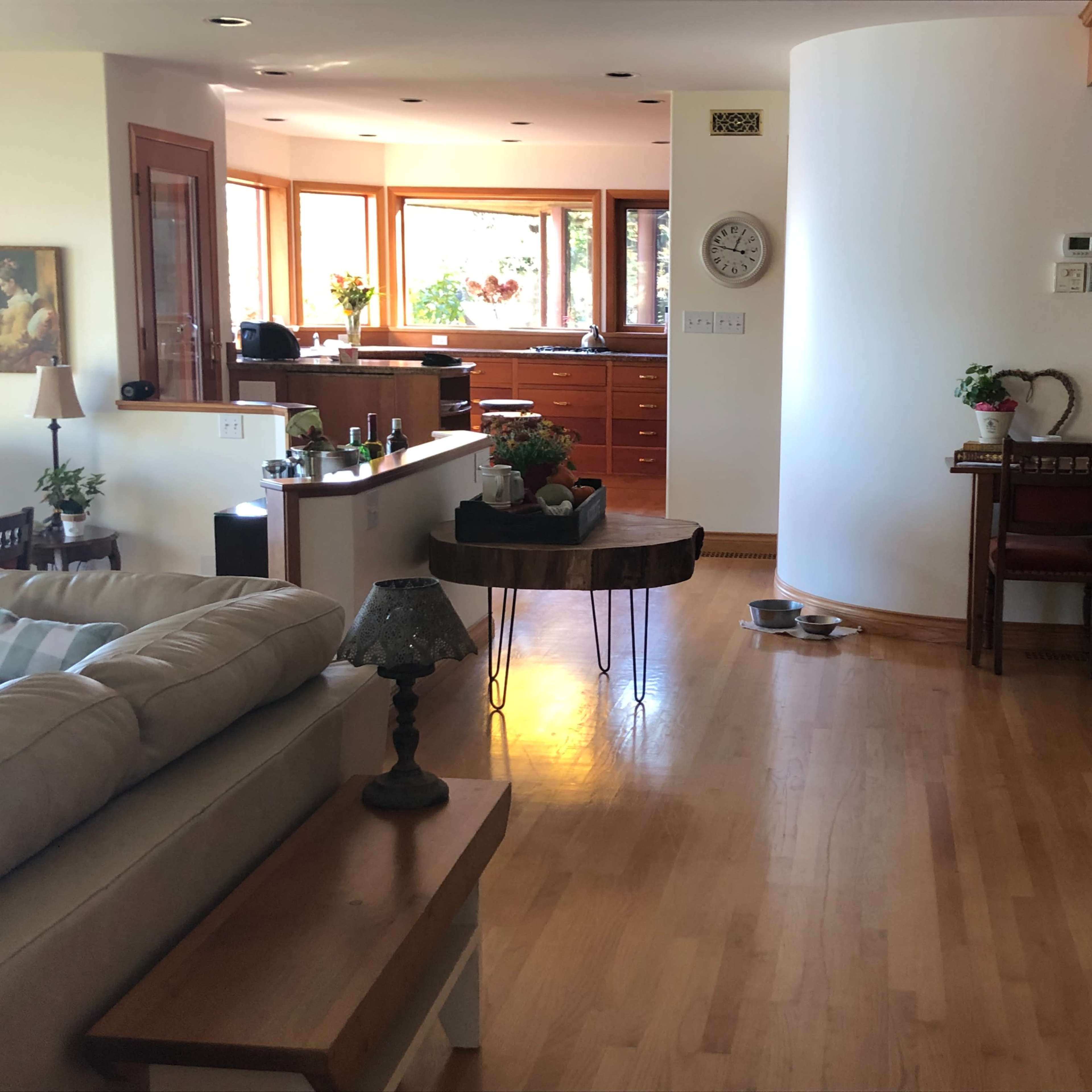 A well-lit interior space featuring a living area with a couch, a dining area with wooden furniture, and a staircase leading to an upper level.