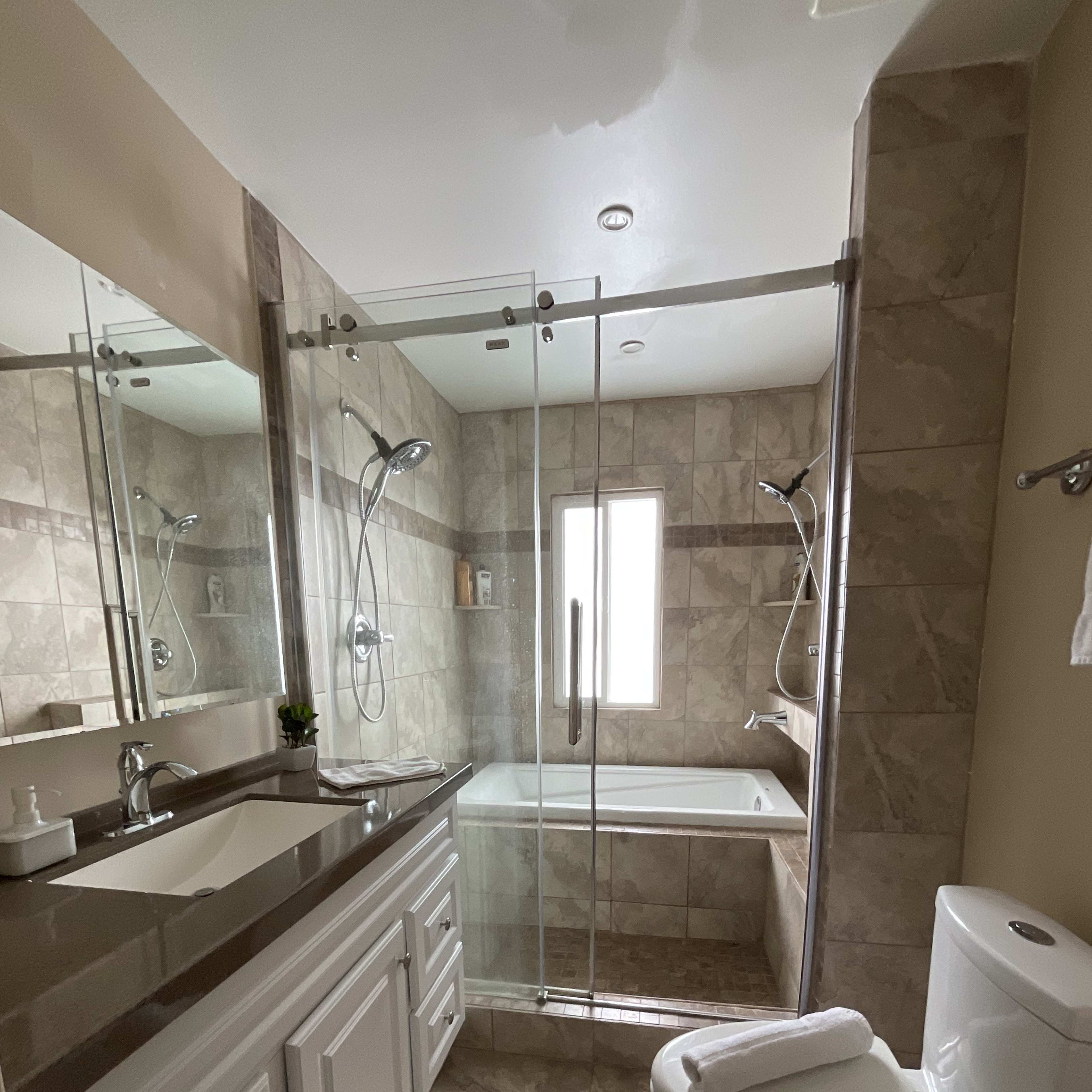 A modern bathroom with a glass shower, a bathtub, a white vanity, and a toilet.