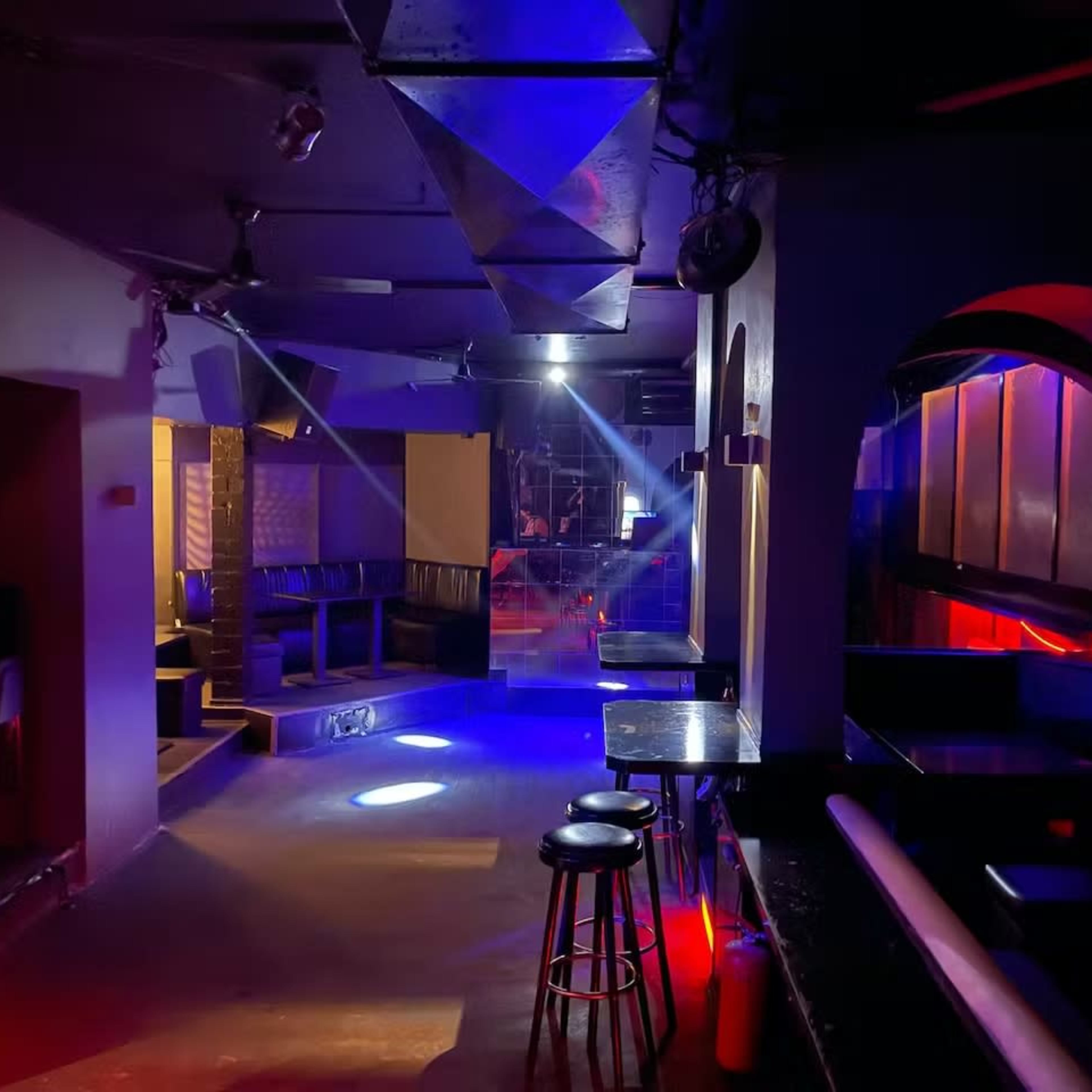 A dimly lit nightclub interior features empty seating areas, polished surfaces, and colorful lighting effects.