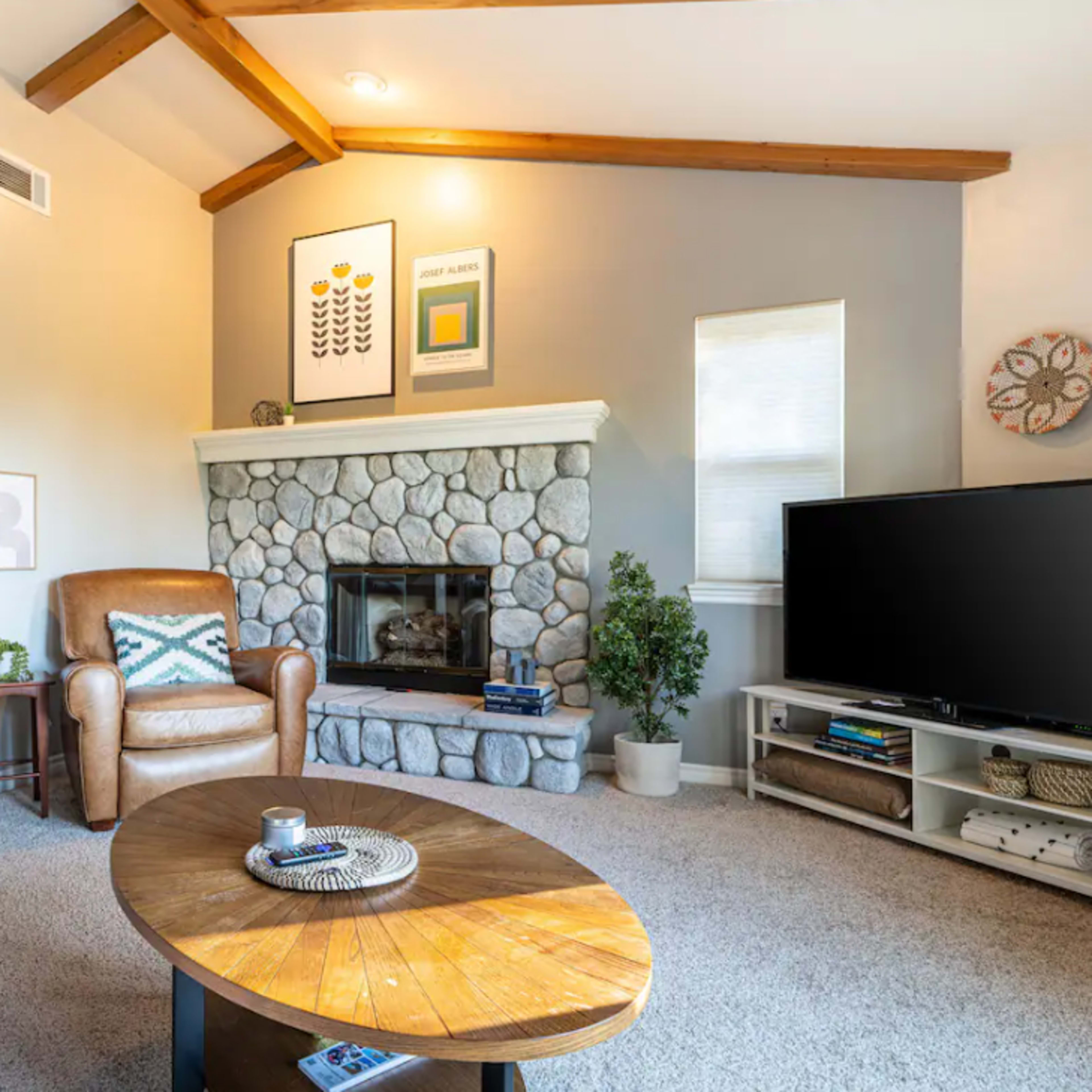The living room features a stone fireplace, a brown leather chair, a gray sofa, and a television on a side table.