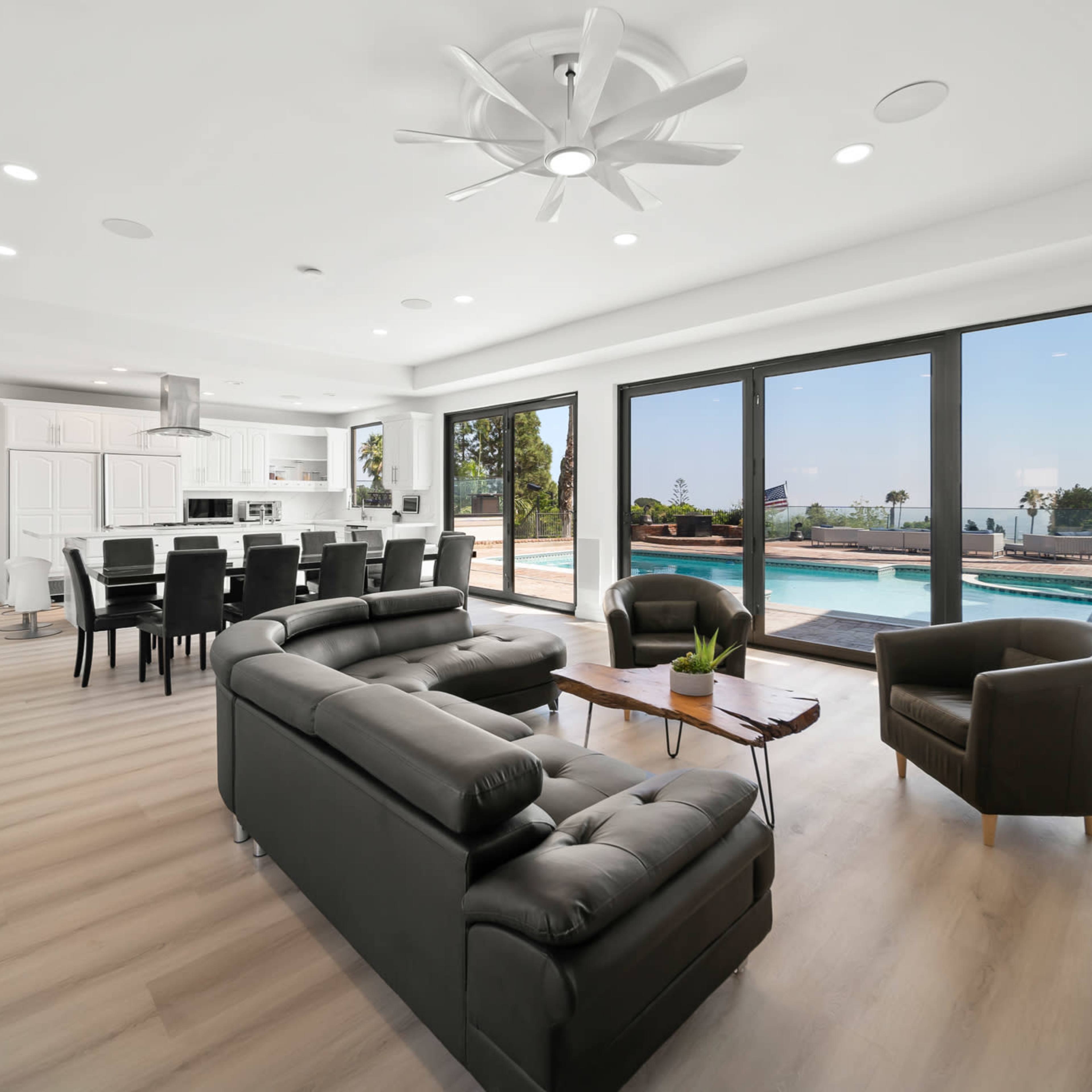 A modern living space with a black sofa, a dining area, and large glass doors opening to a poolside view.