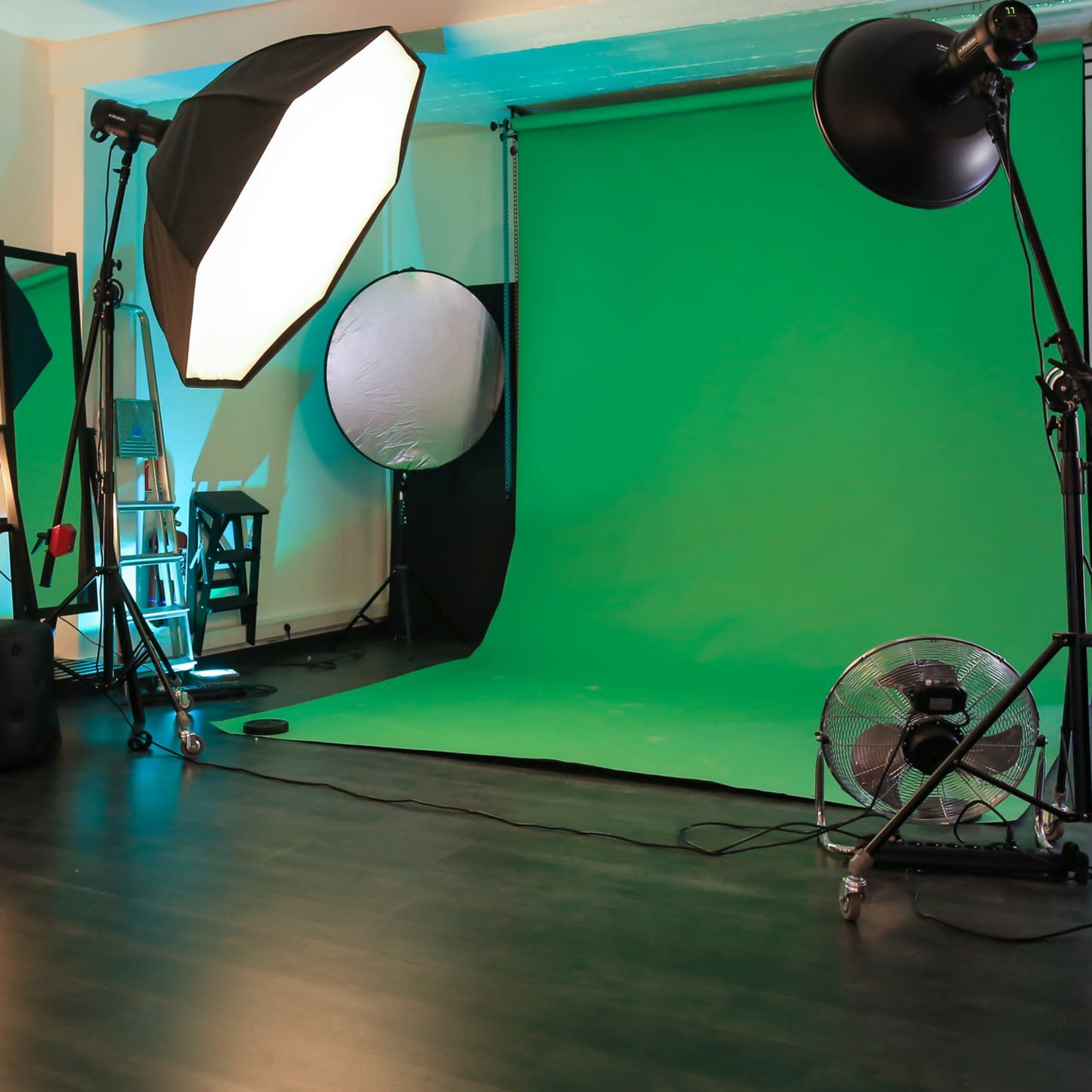 A photo studio setup with a green backdrop, lighting equipment, and a computer on a table.