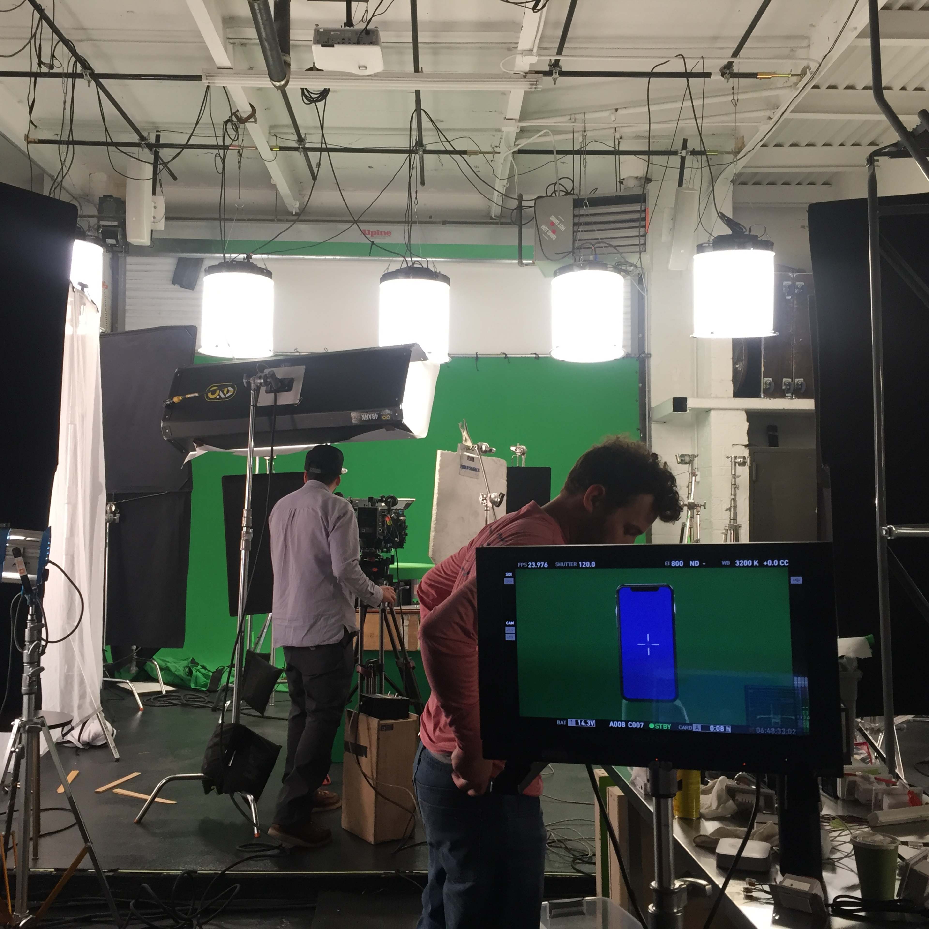 A film studio setup with a green screen background, several lights, and crew members preparing equipment.