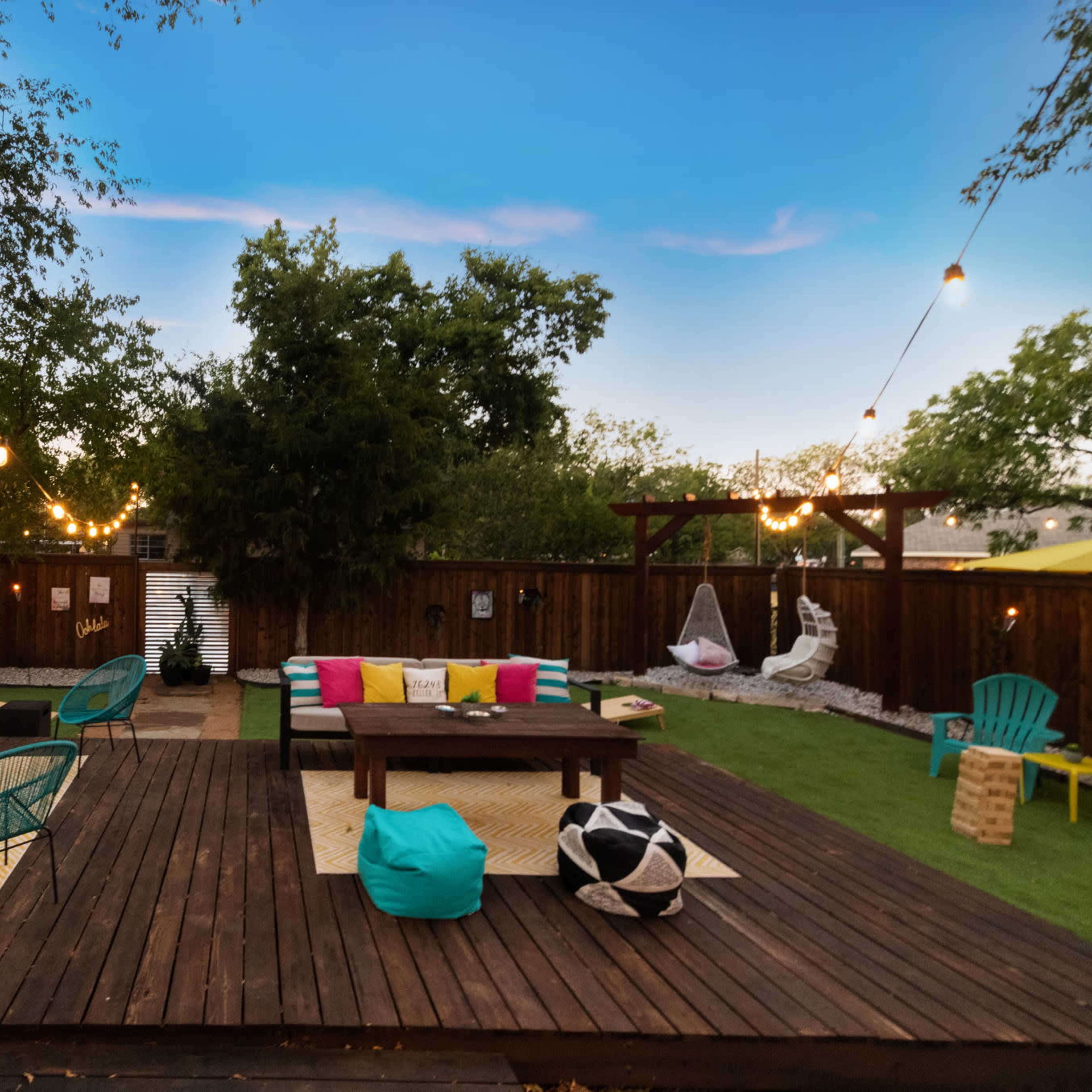 A spacious outdoor patio area with wooden decking, colorful lounge furniture, and decorative lighting strung across the space.