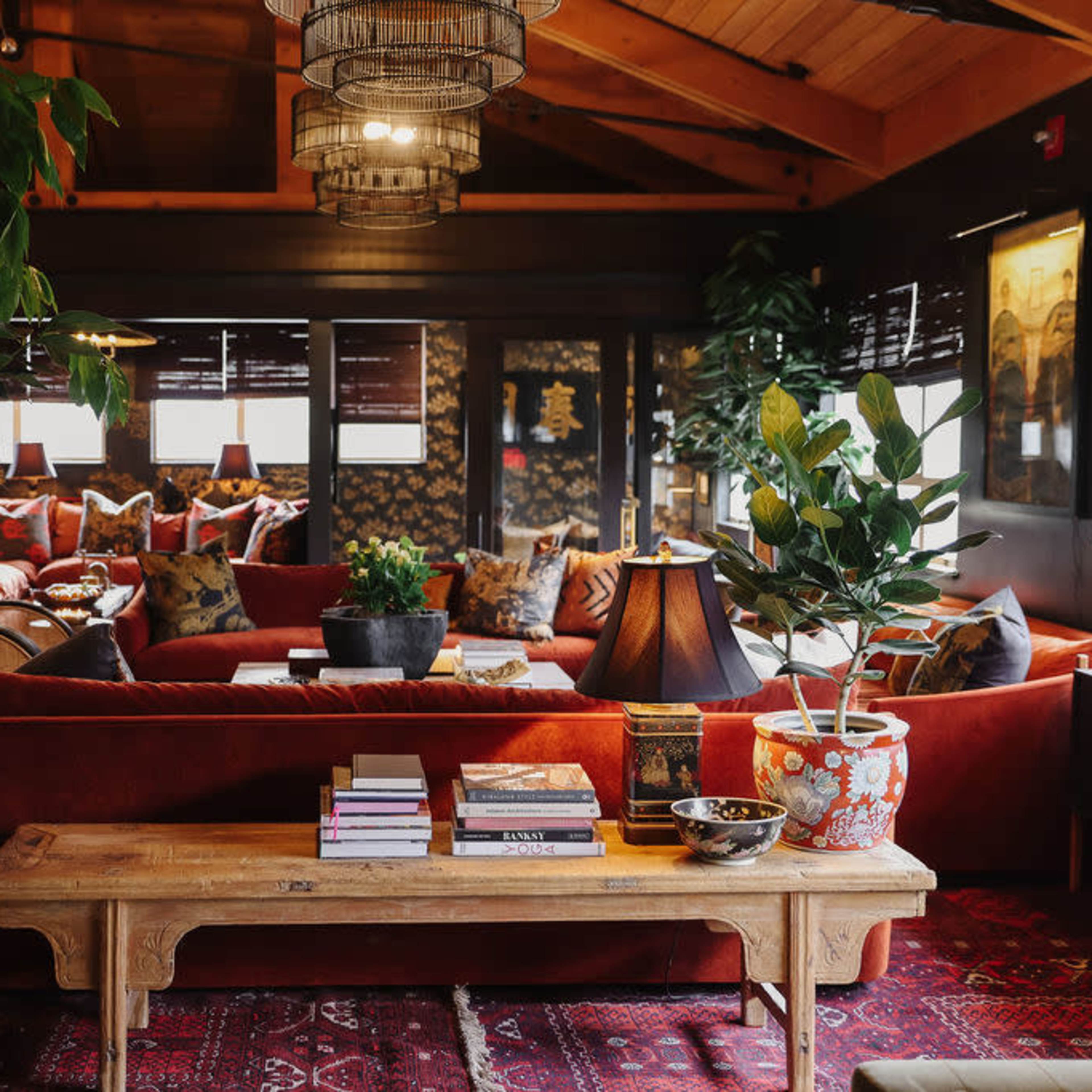 A cozy living room filled with plush seating, plants, and a wooden coffee table adorned with books and decorative items.