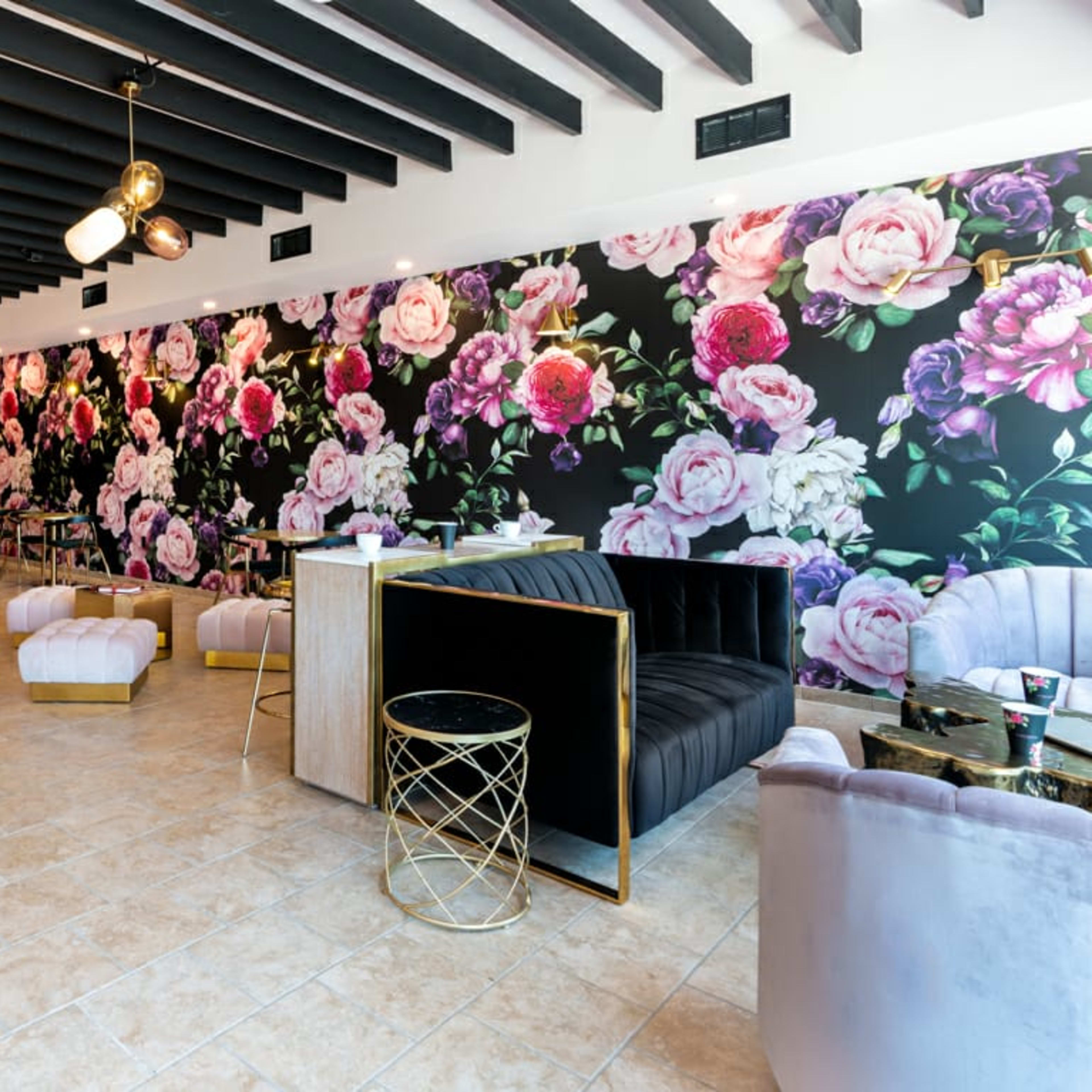 A modern café interior with a floral wallpaper, elegant seating arrangements, and gold accents.