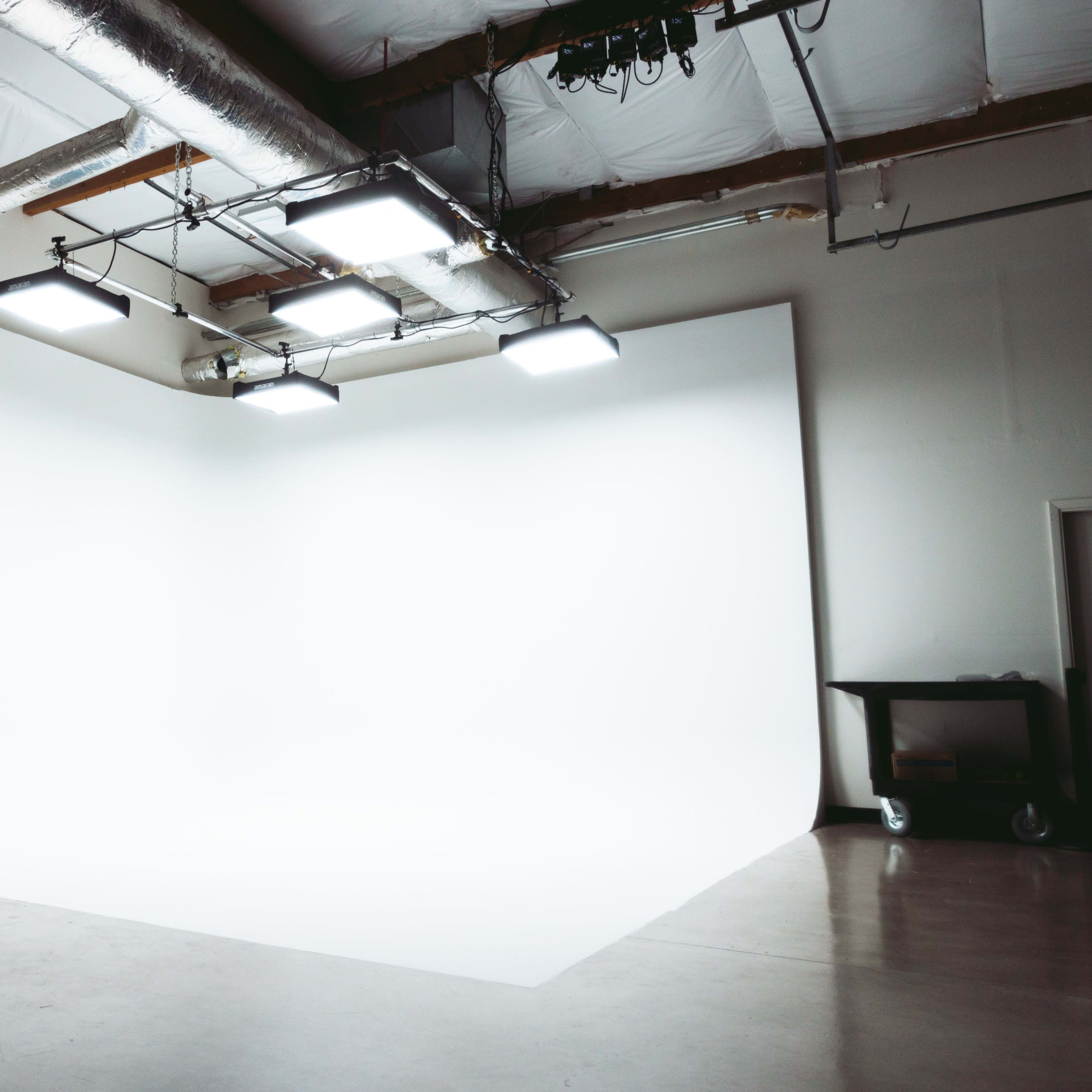 An empty photography studio with a seamless white backdrop and overhead lighting.