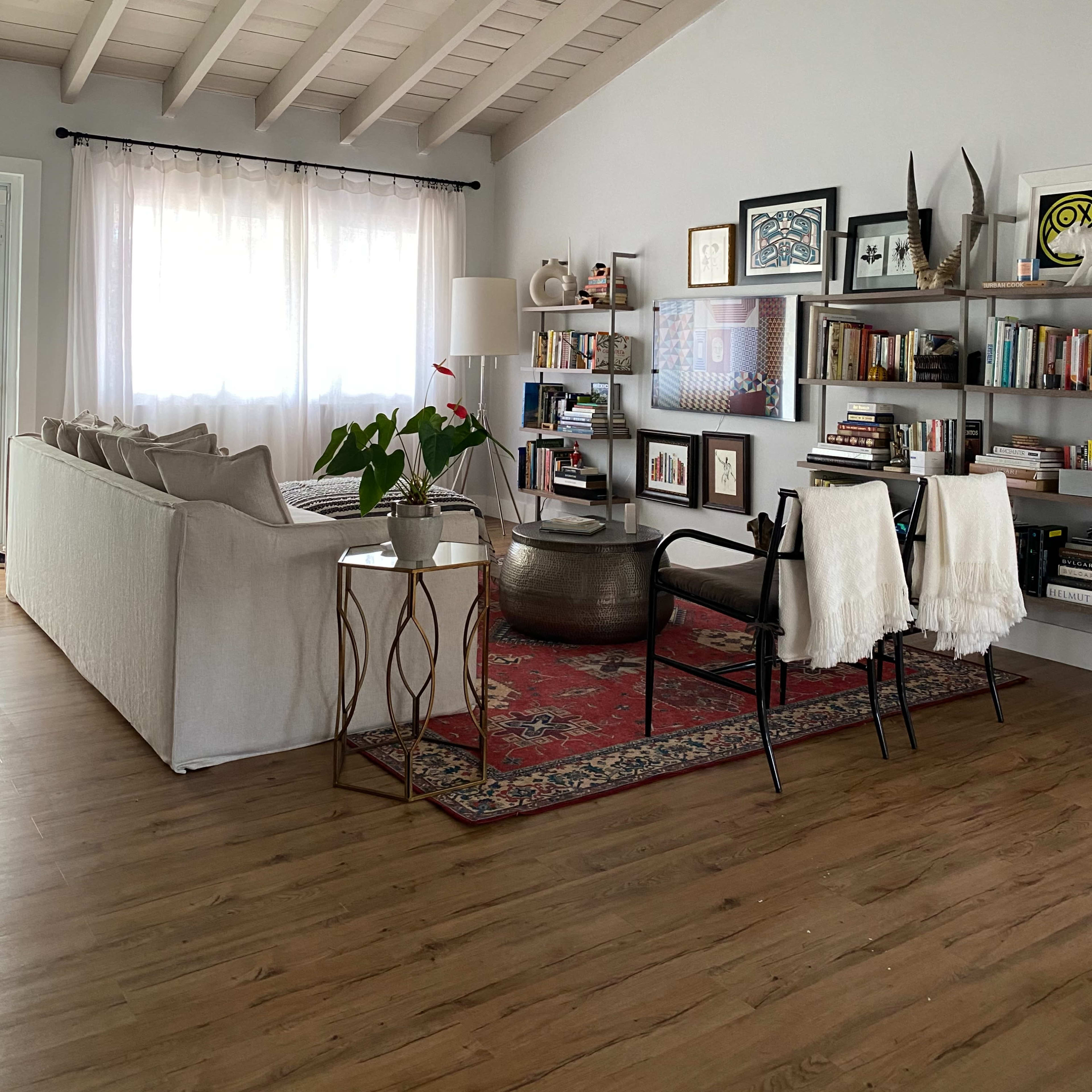 A modern living room with a light-colored sofa, a round coffee table, bookshelves, and a patterned area rug under a chandelier.