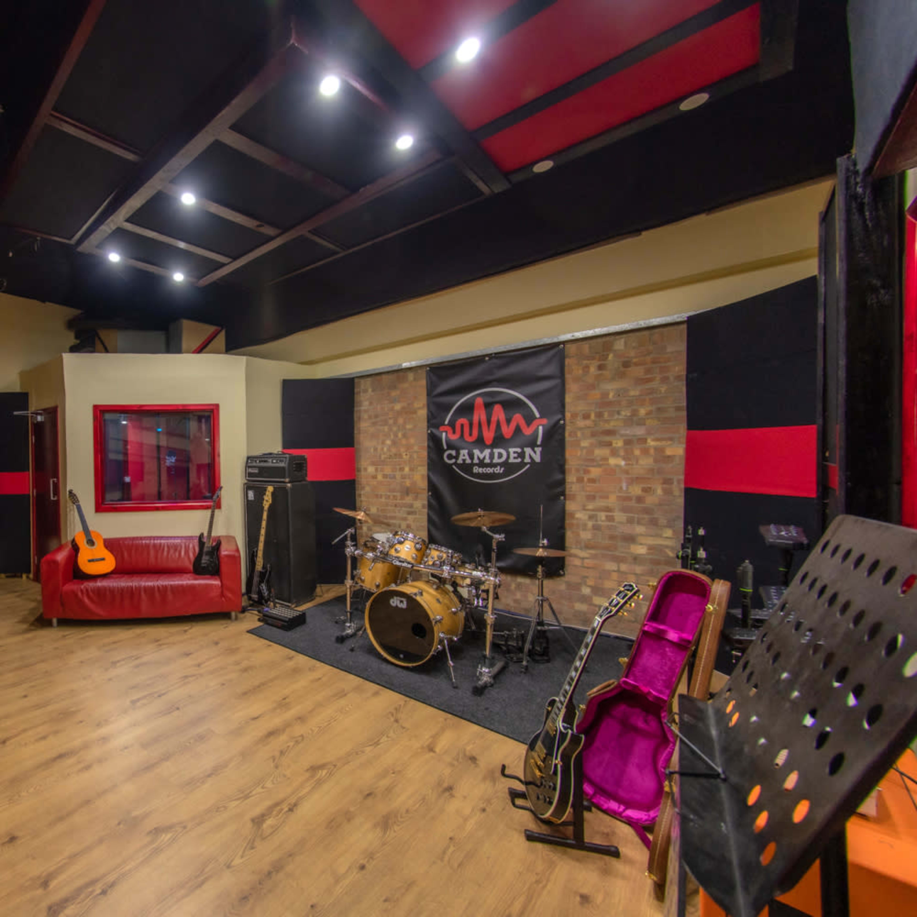 A music studio with a red and black color scheme, featuring a seating area, a drum set, and various instruments against a textured wall.