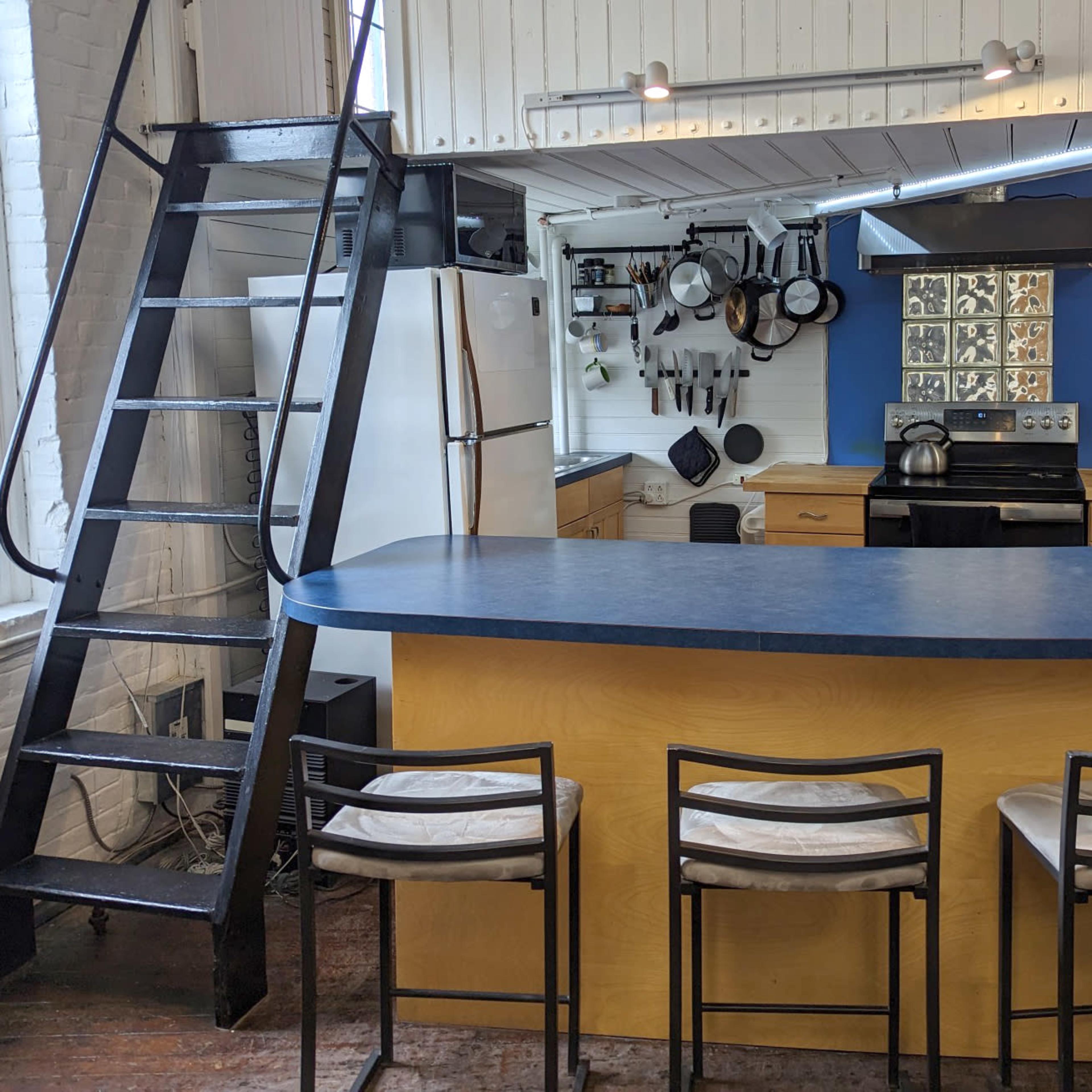 A kitchen with a bar seating area and a metal ladder leading to a loft space.