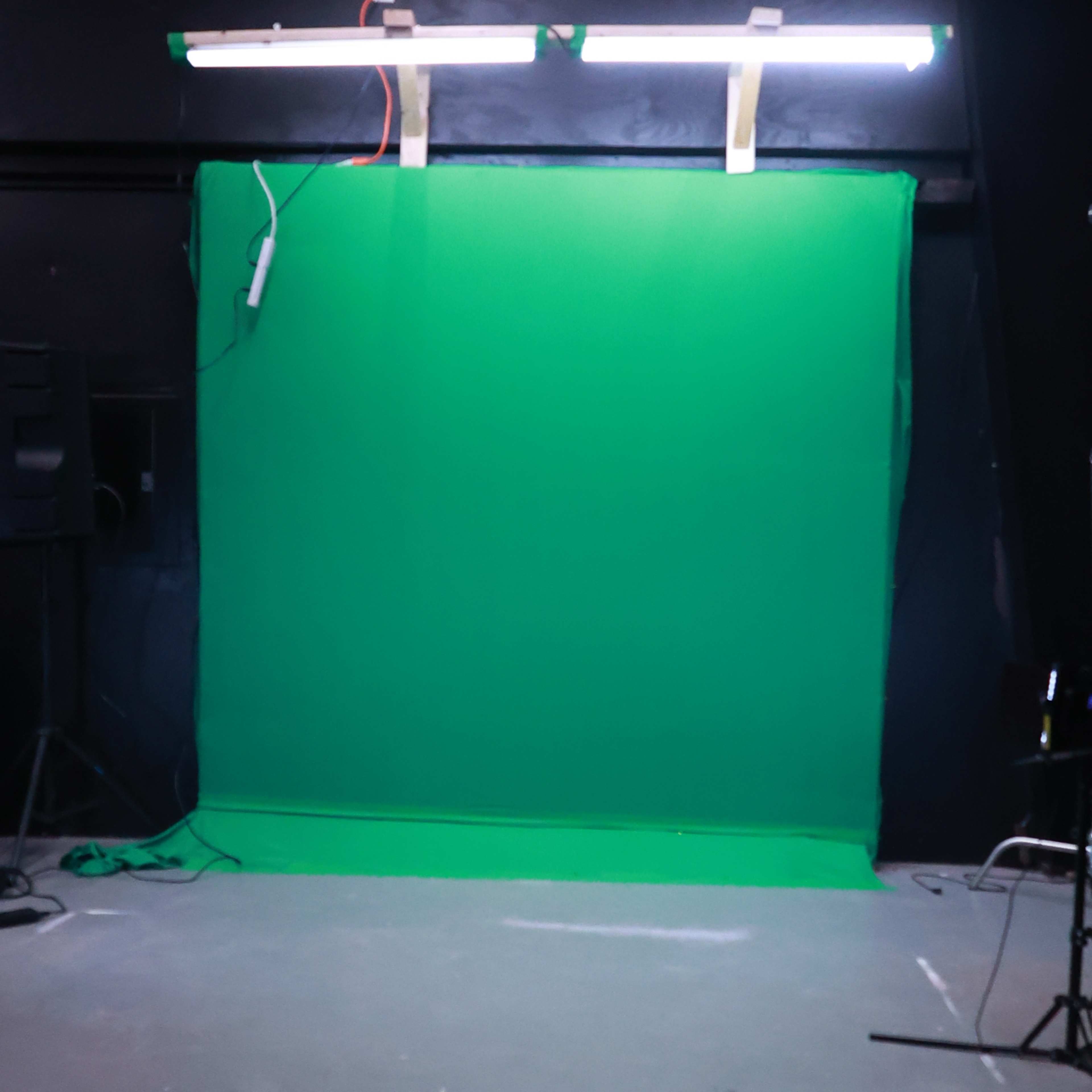 A green screen setup in a studio with overhead lights and an empty space in front.