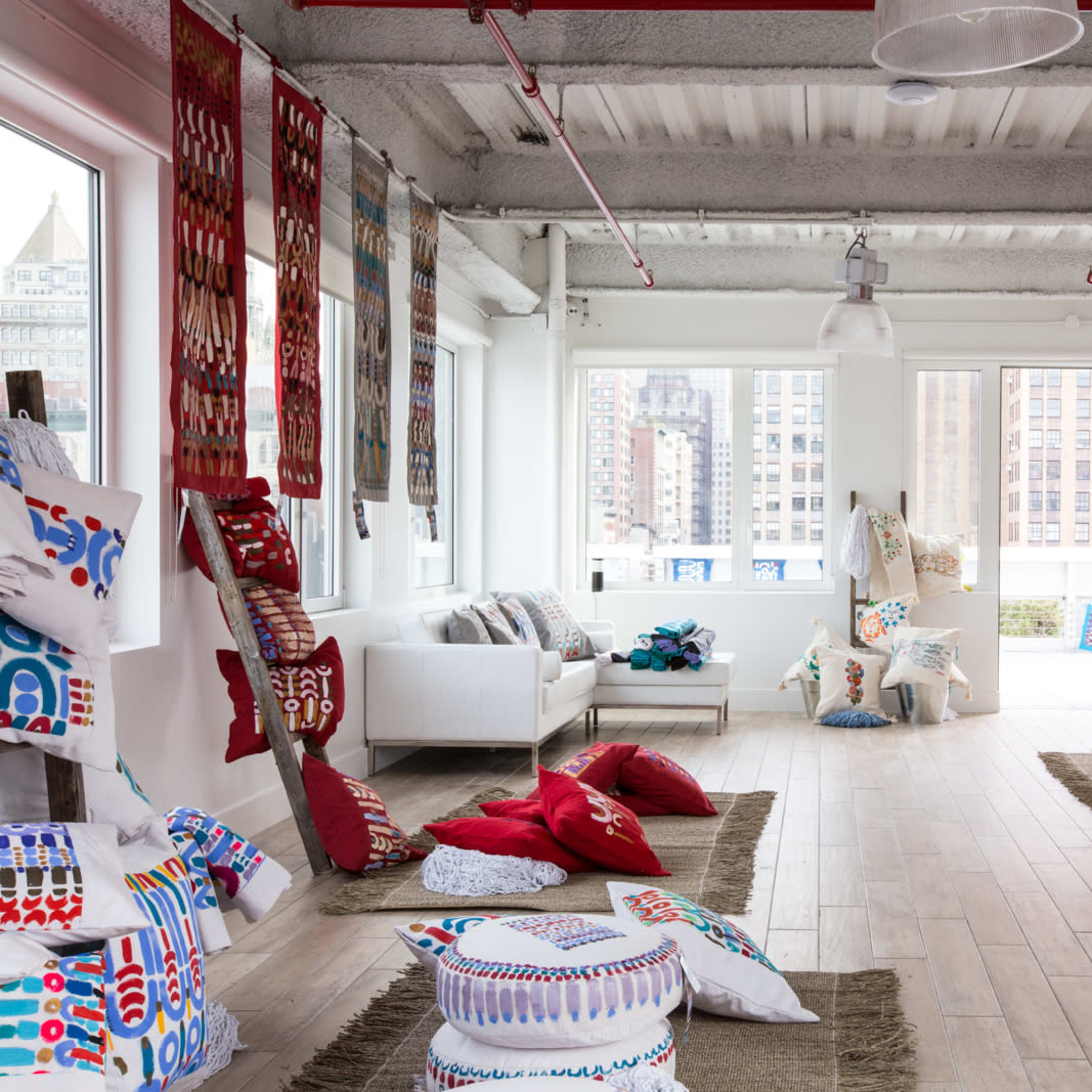 A spacious room filled with colorful pillows and decorative textiles, featuring large windows that allow natural light to illuminate the space.