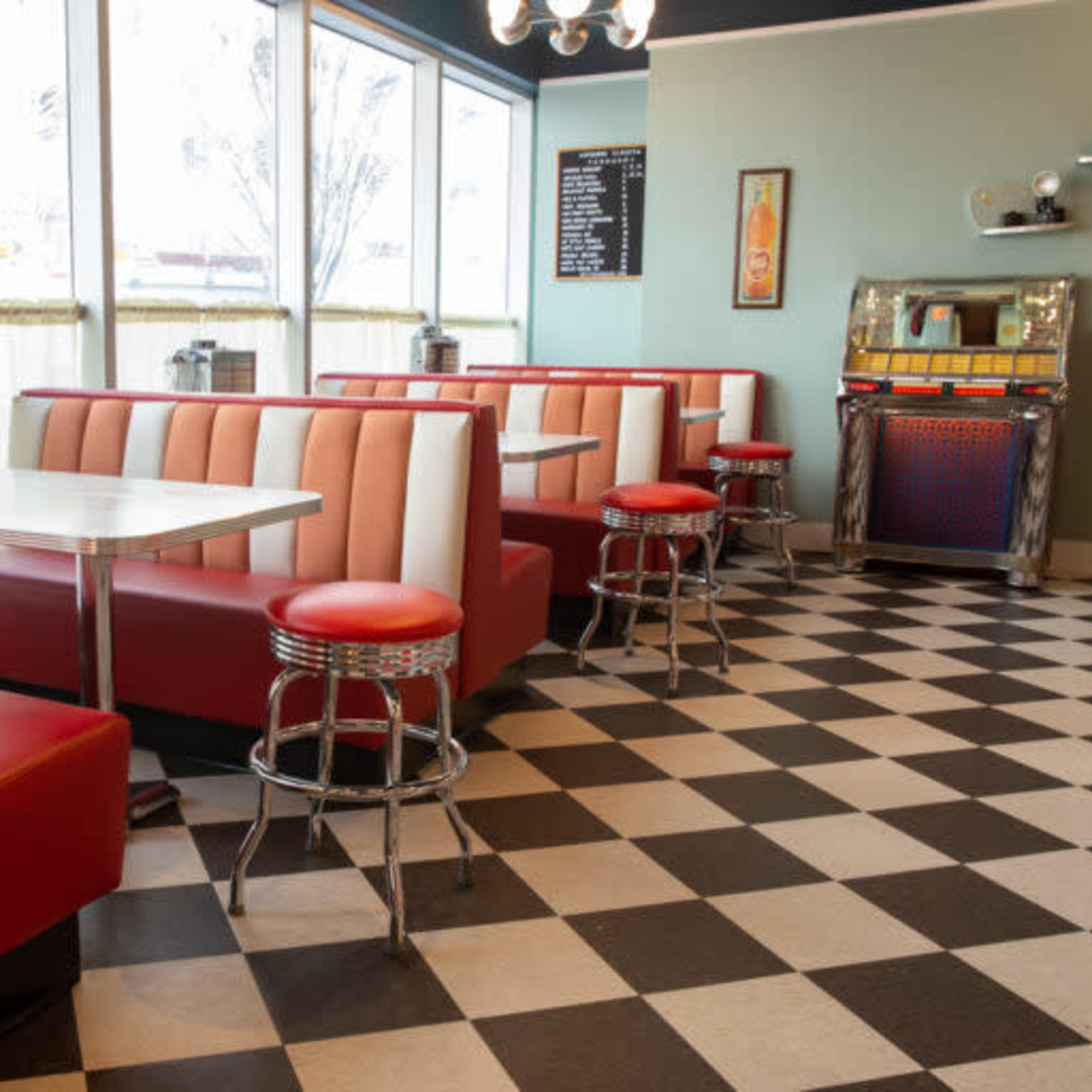 A retro-style diner with red and white vinyl booths, chrome stools, and a black and white checkered floor.