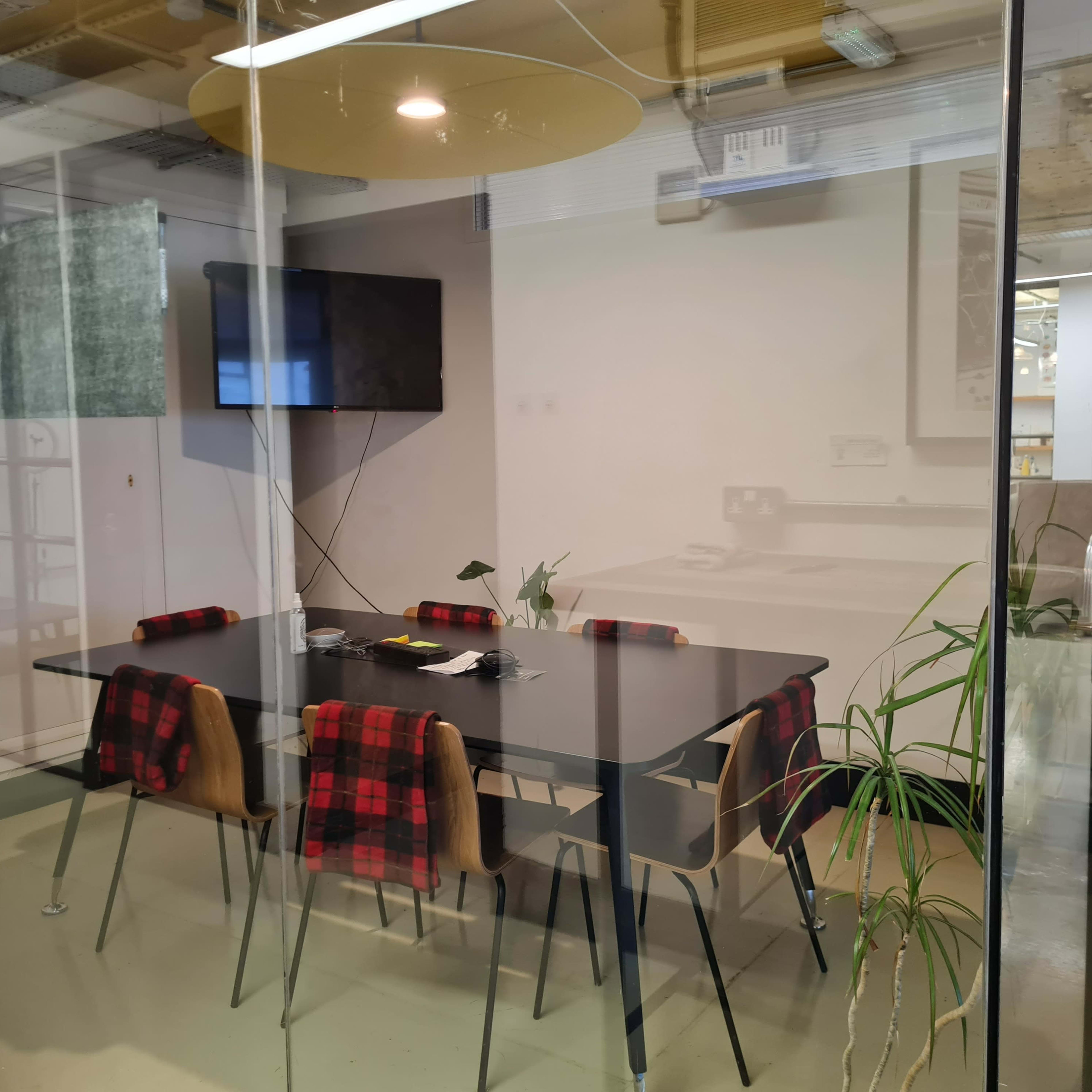 A conference room features a glass wall, a black table surrounded by chairs, and a wall-mounted television.
