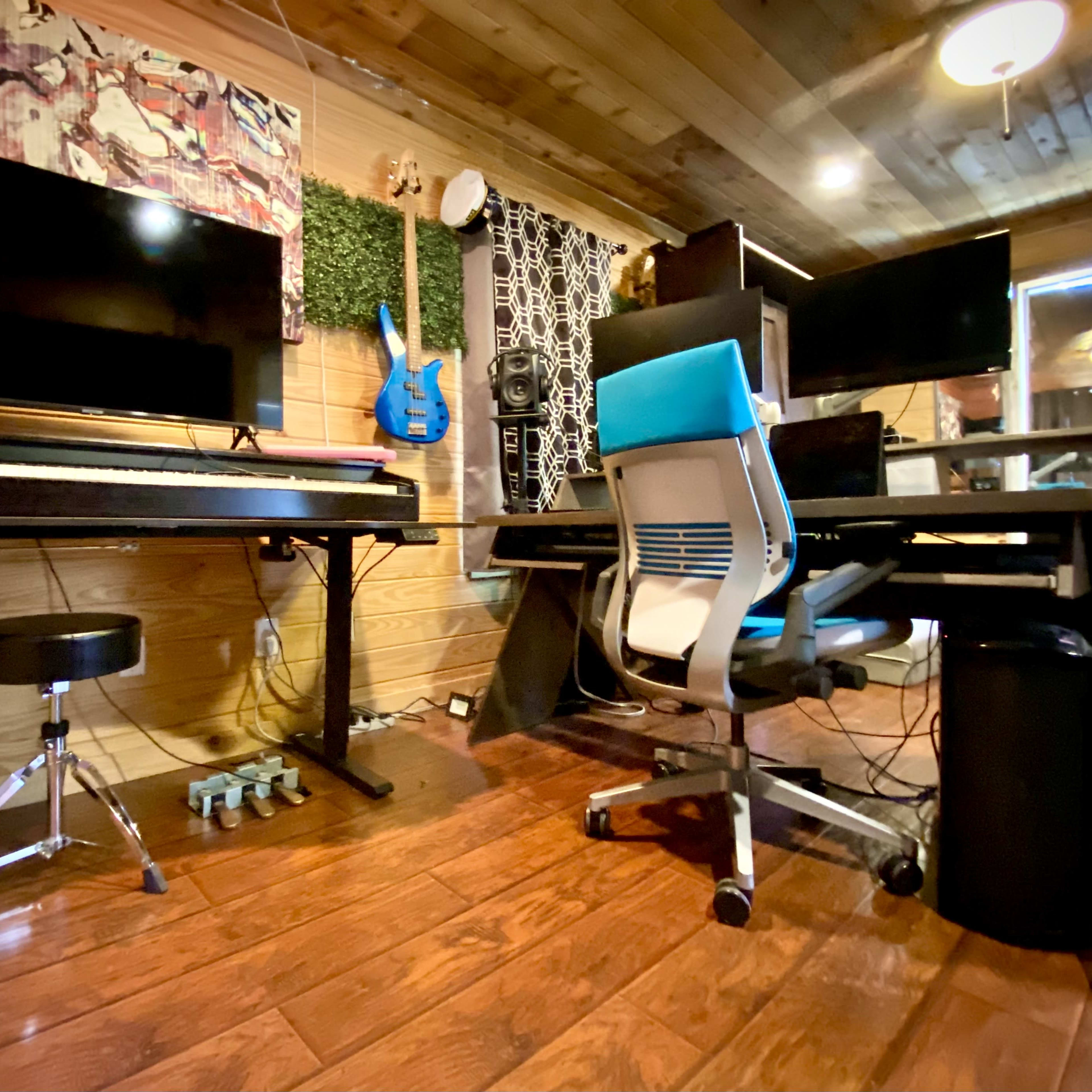 A music production studio with a digital piano, multiple monitors, a colorful guitar, and a modern office chair.