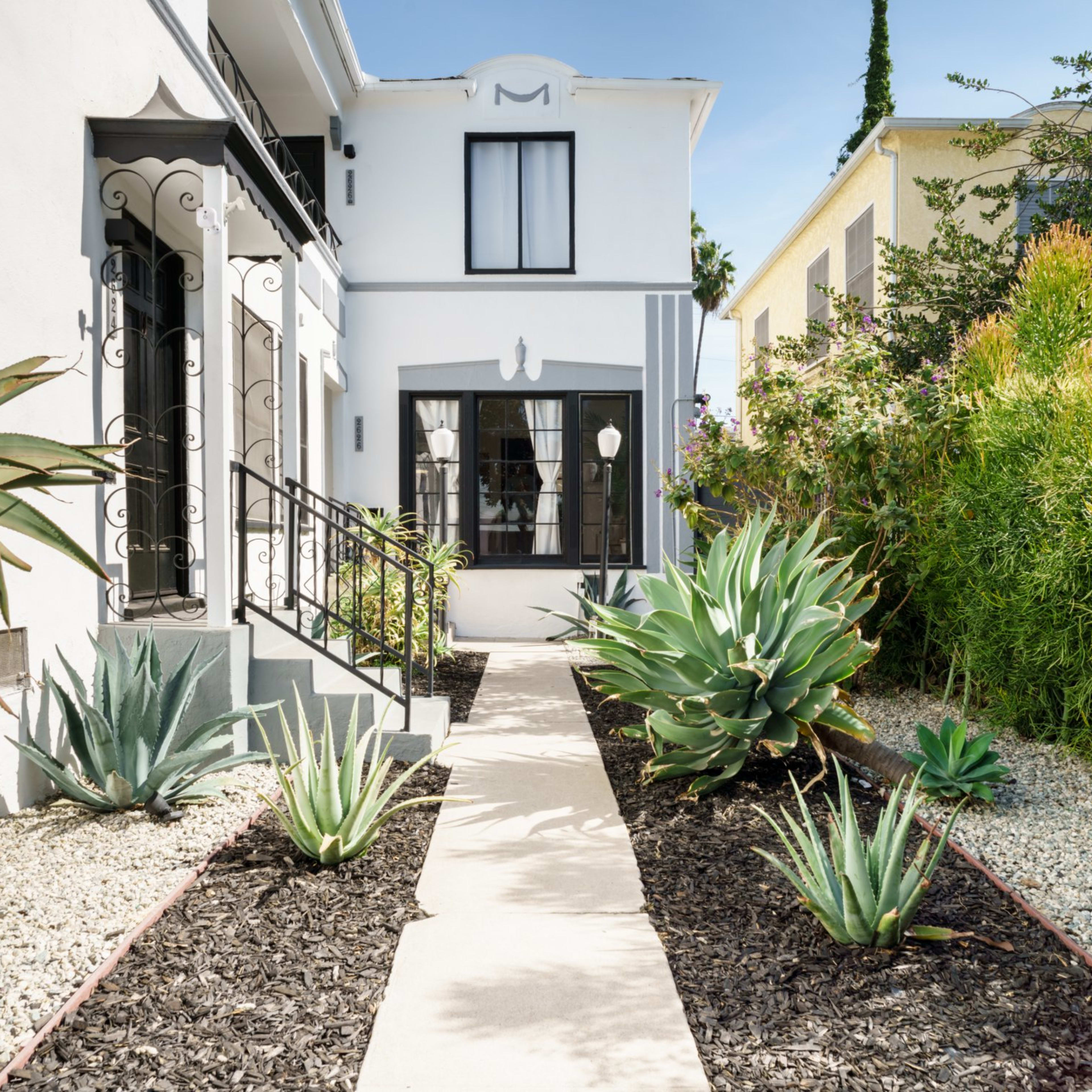 A pathway leading to a white house, bordered by decorative plants and gravel landscaping on either side.